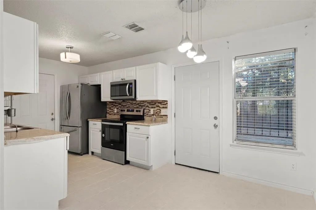 Kitchen featuring white cabinetry, stainless steel appliances, a tile backsplash, and light-toned tile flooring