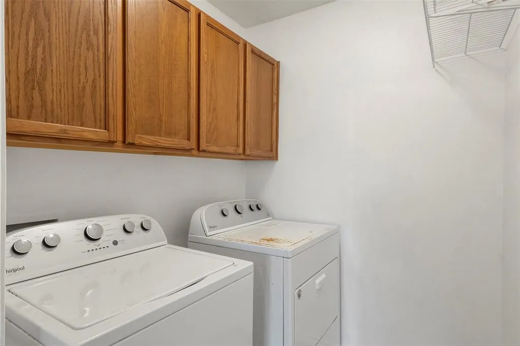 Upper wood-finish cabinetry, white washer and dryer units, and wire shelving