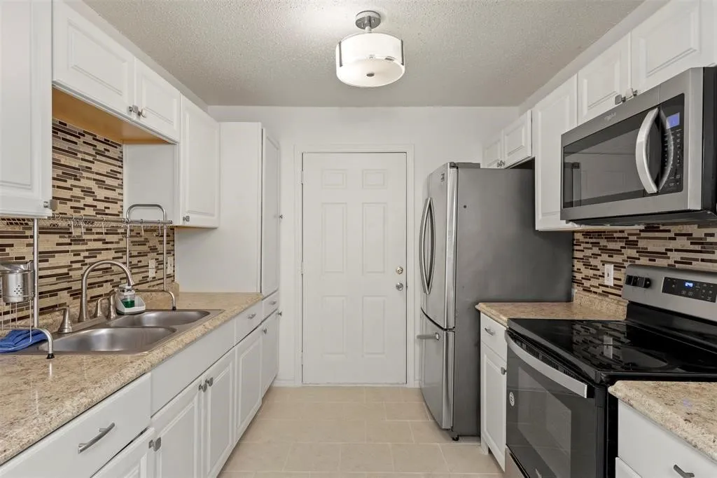 White cabinetry, mosaic tile backsplash, double basin sink, stainless steel appliances, and neutral-toned flooring