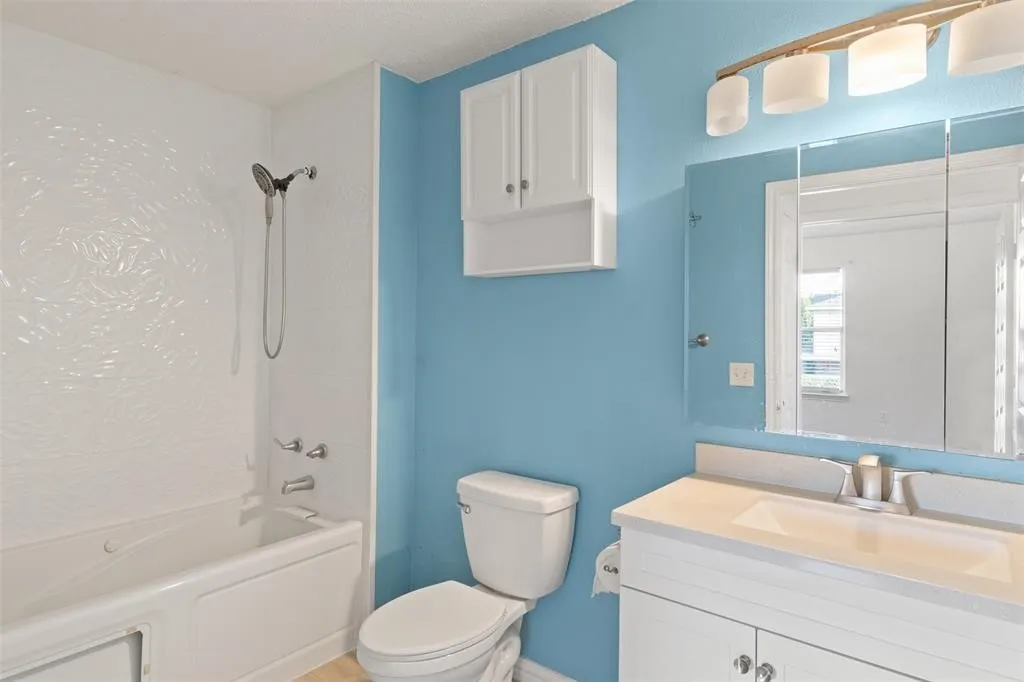 White bathtub with patterned shower surround, light blue wall paint, white vanity with integrated sink, mirrored medicine cabinet, and white wall-mounted cabinet