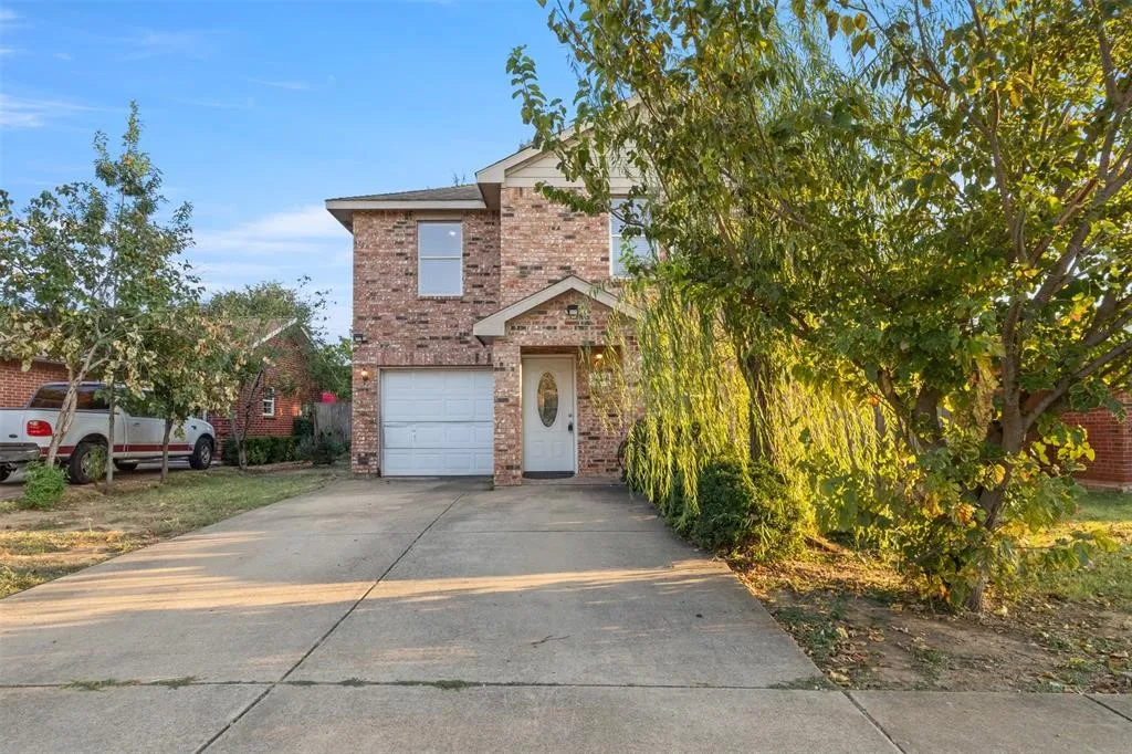 Brick facade residence featuring an attached garage, paved driveway, and mature landscaping
