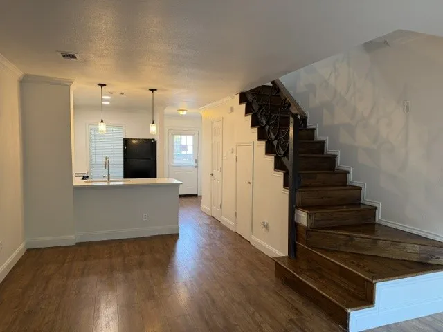 Wood-finish flooring throughout, kitchen island with sink and pendant lighting, built-in cabinetry, and a staircase with decorative wrought iron railing