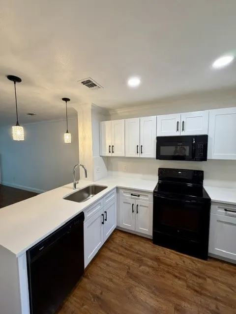 Kitchen featuring wood-finish flooring, white cabinetry, a stainless steel sink, black appliances, and pendant lighting