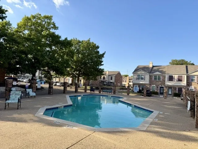 Gated pool area featuring a freeform pool, surrounding textured concrete decking, and mature trees