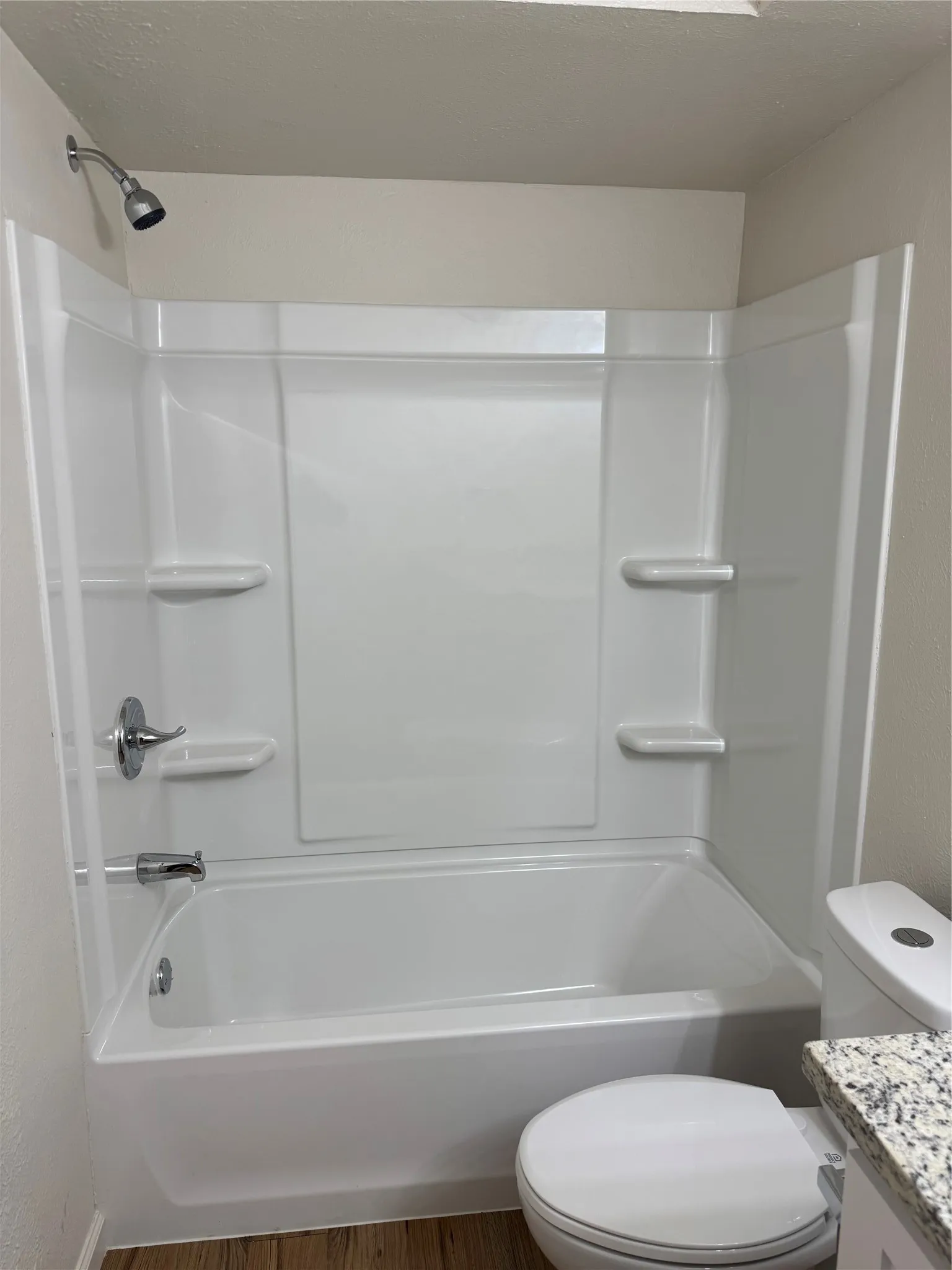 White bathtub with shower head, built-in soap dishes, and wood-finish flooring