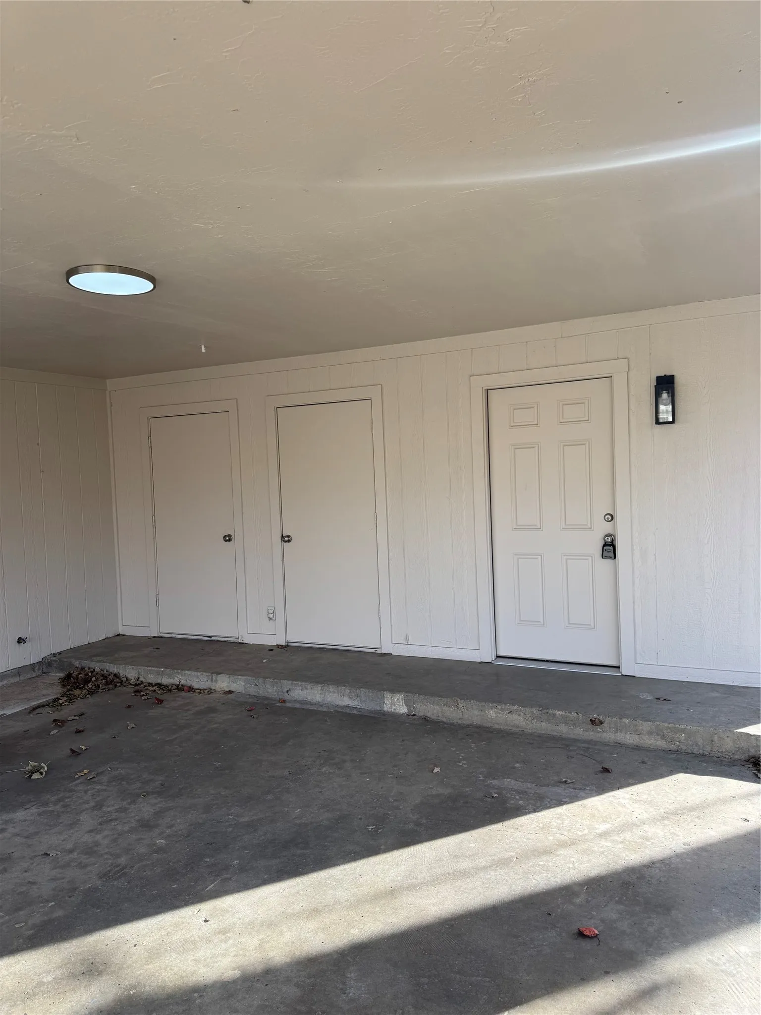Covered concrete patio area featuring multiple storage doors, a paneled entry door, and a flush-mount overhead light