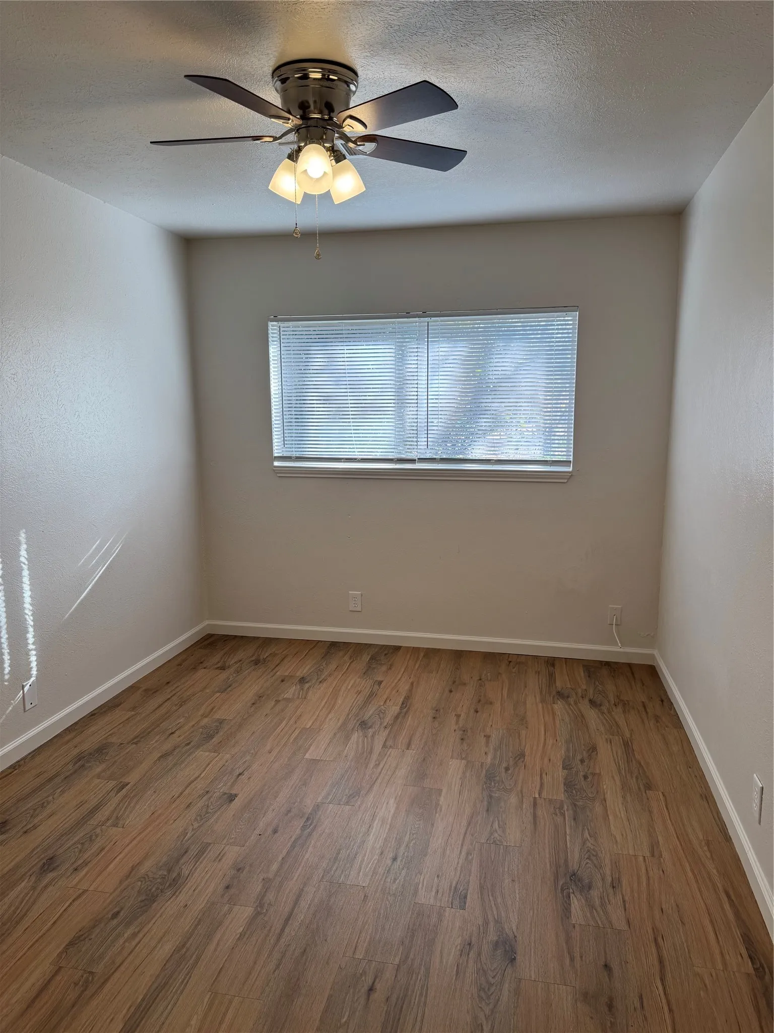 Wood-finish flooring with white baseboards, a ceiling fan with integrated lighting, and a window with blinds