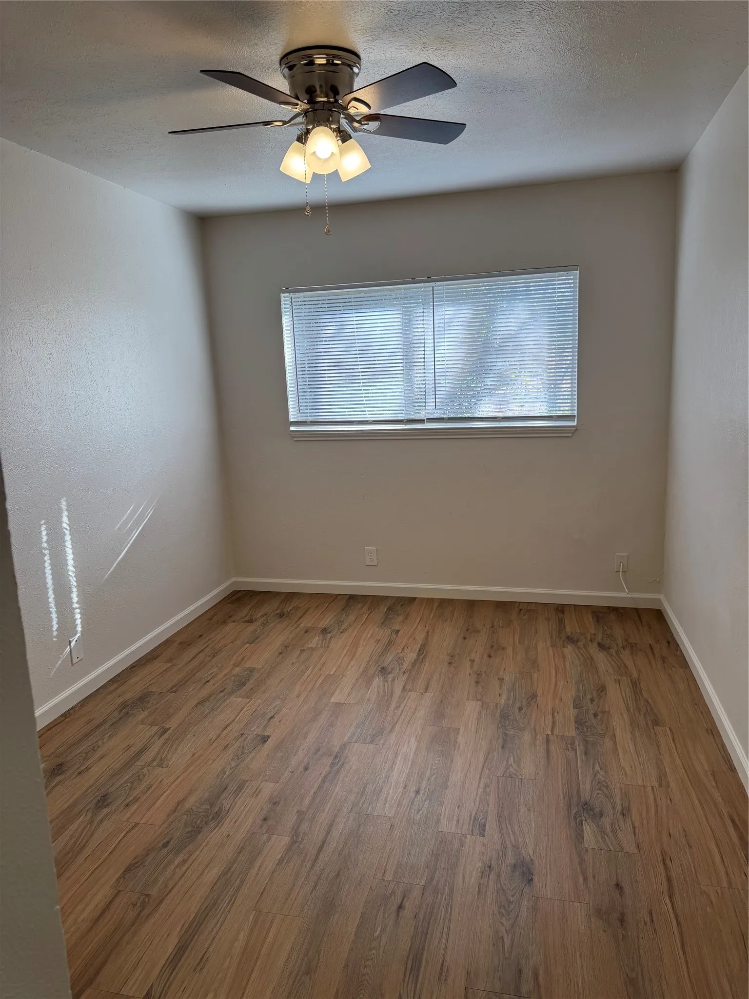 Wood-finish flooring throughout, ceiling fan with integrated lighting, and a window with horizontal blinds