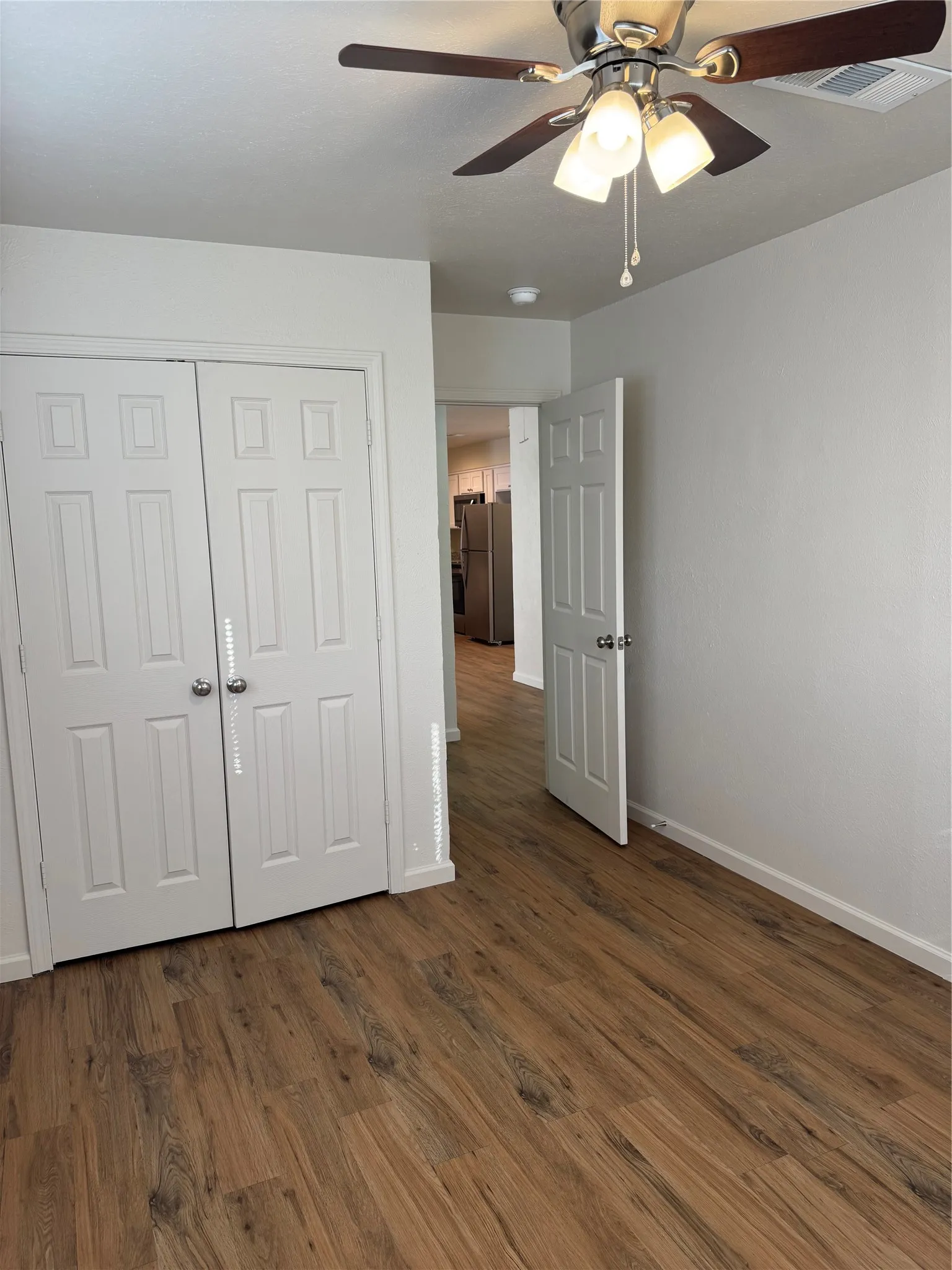Wood-finish flooring throughout, bright white walls, and a ceiling fan with integrated lighting
