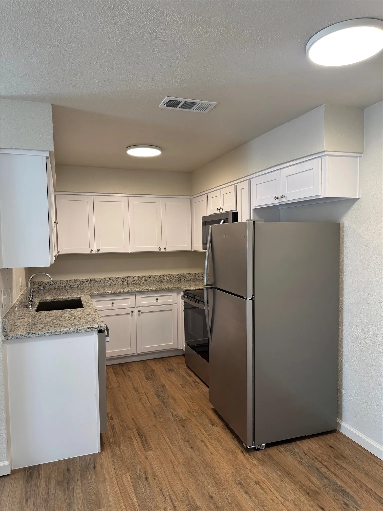 Kitchen featuring wood-finish flooring, white cabinetry, integrated stainless steel appliances, and solid surface countertops