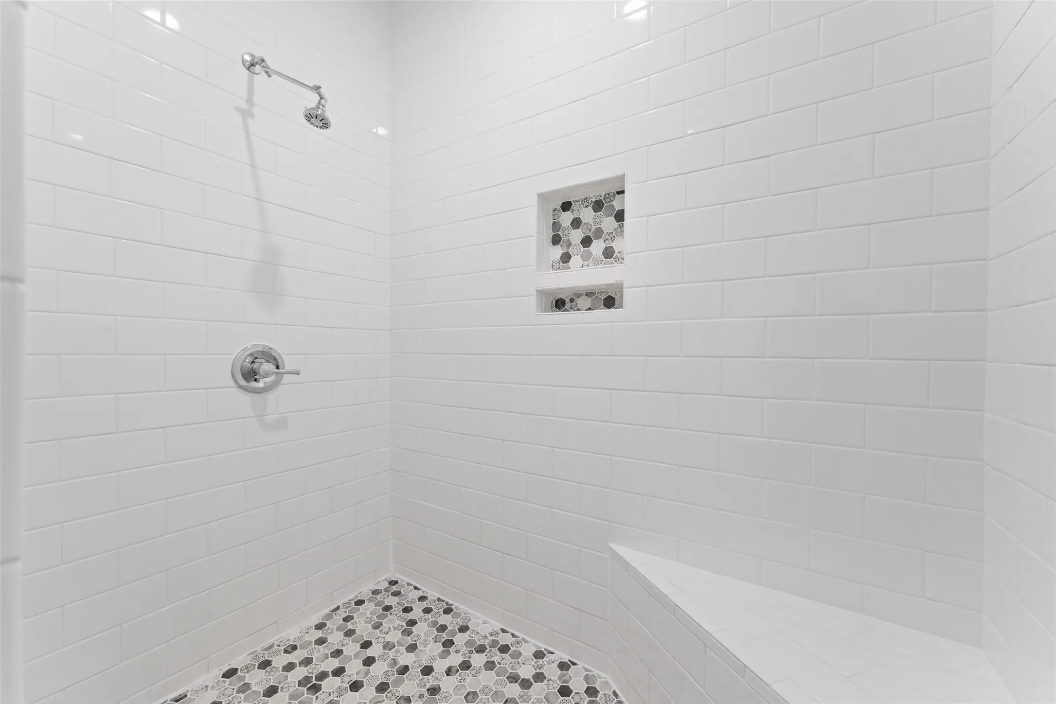 Shower featuring subway tile walls, a built-in bench, dual recessed niches with mosaic tile accents, and a hexagonal mosaic tile floor