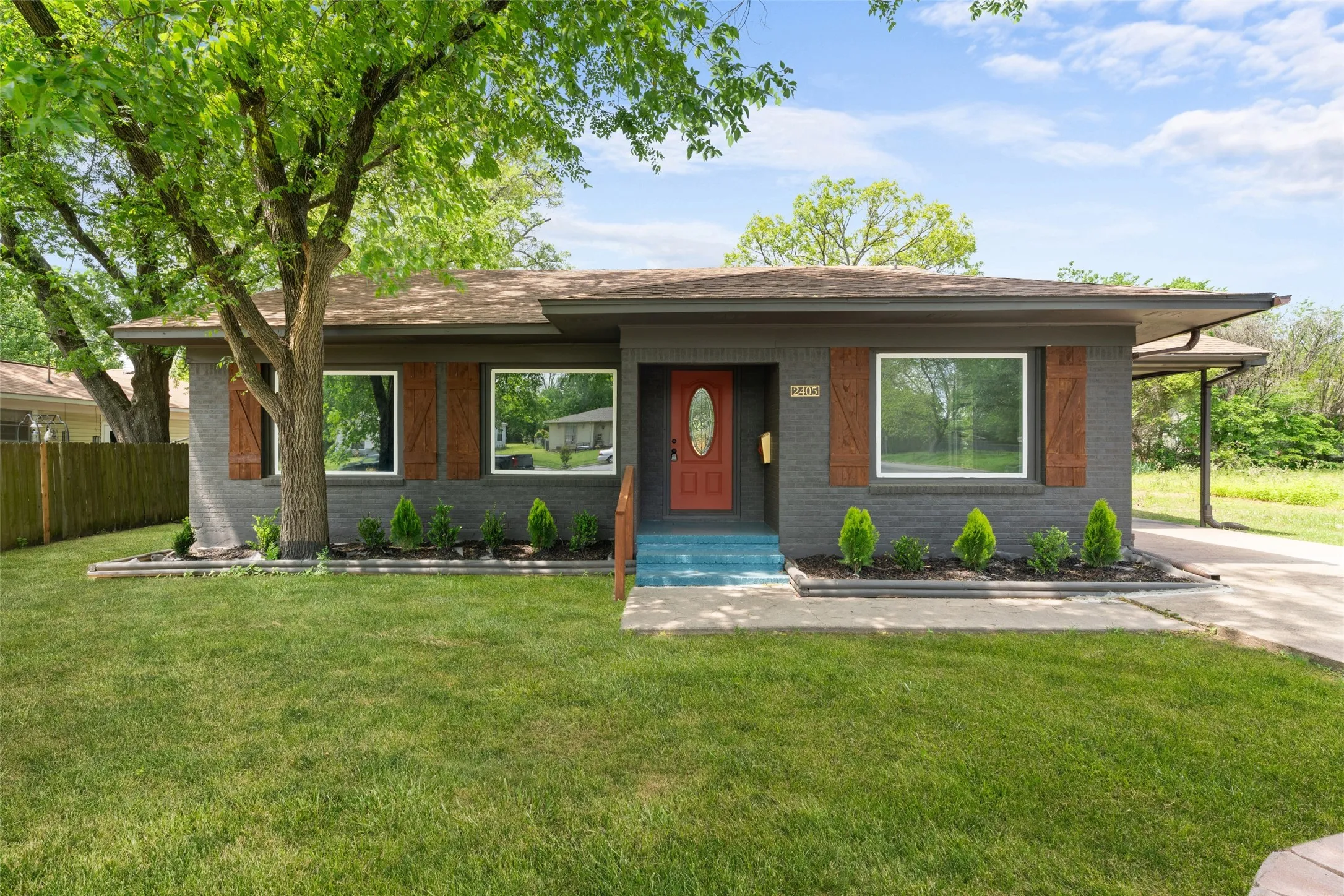 Painted brick exterior with contrasting wood shutters, a vibrant red entry door, a covered carport, and a well-maintained front lawn