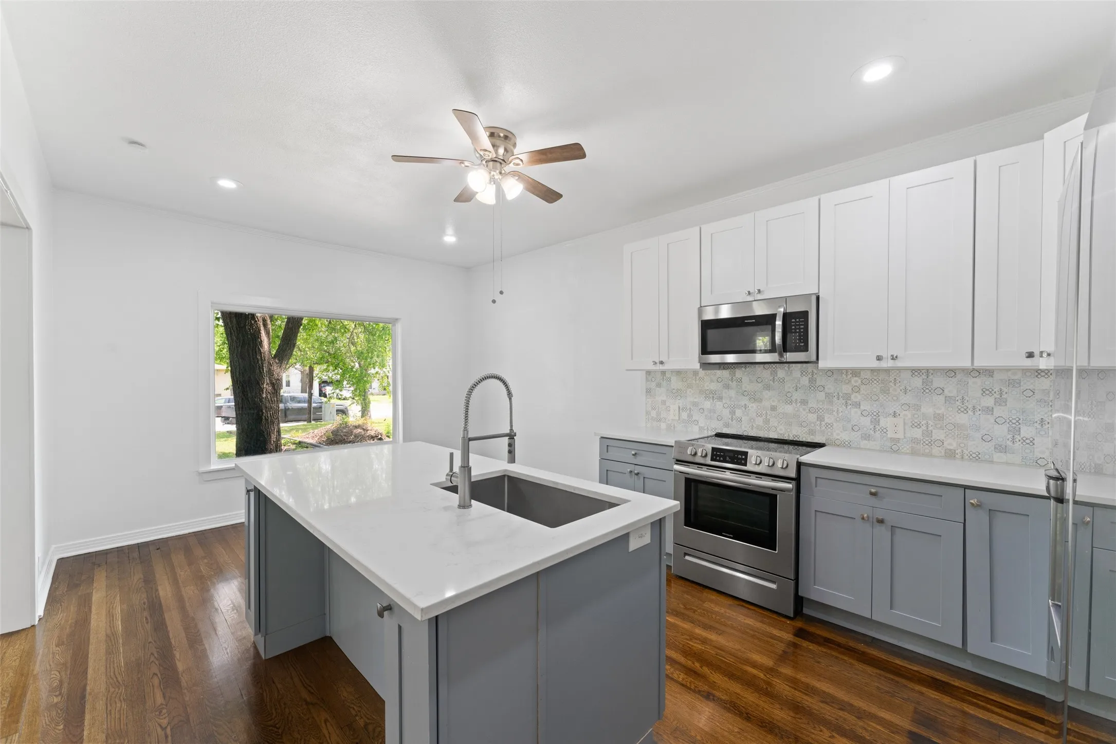 Kitchen featuring a central island with an undermount sink, stainless steel appliances, two-tone cabinetry, and wood-finish flooring