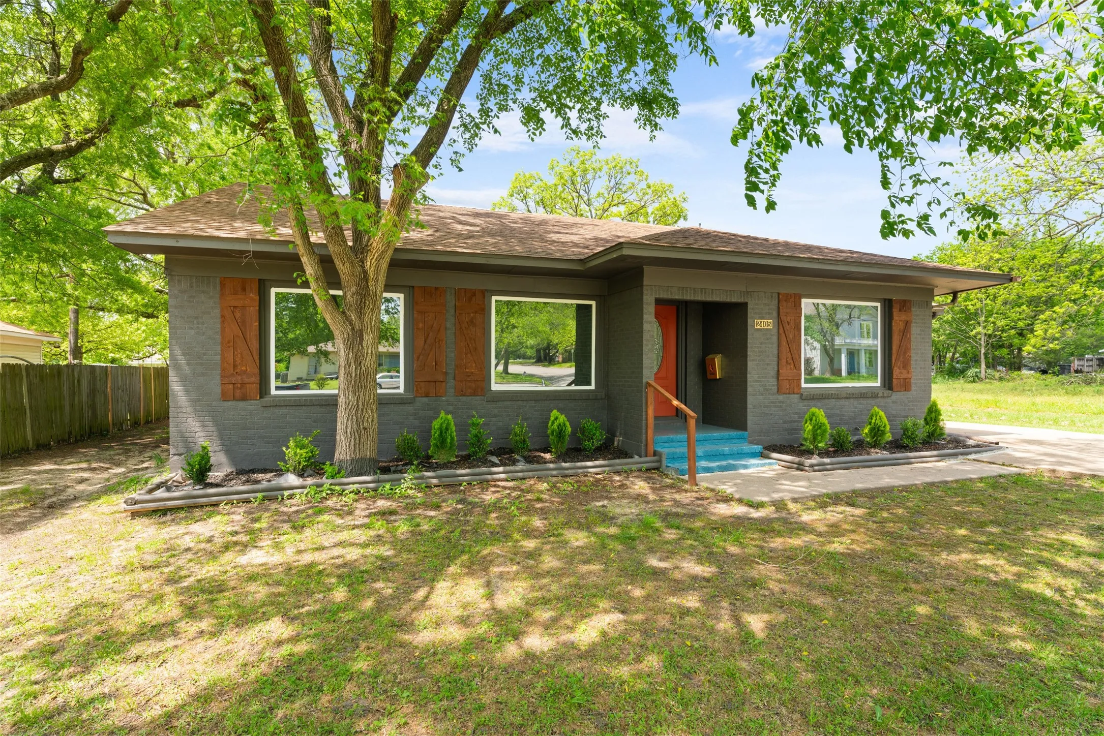 Brick exterior with a shingle roof, wood shutters, and a vibrant entry door