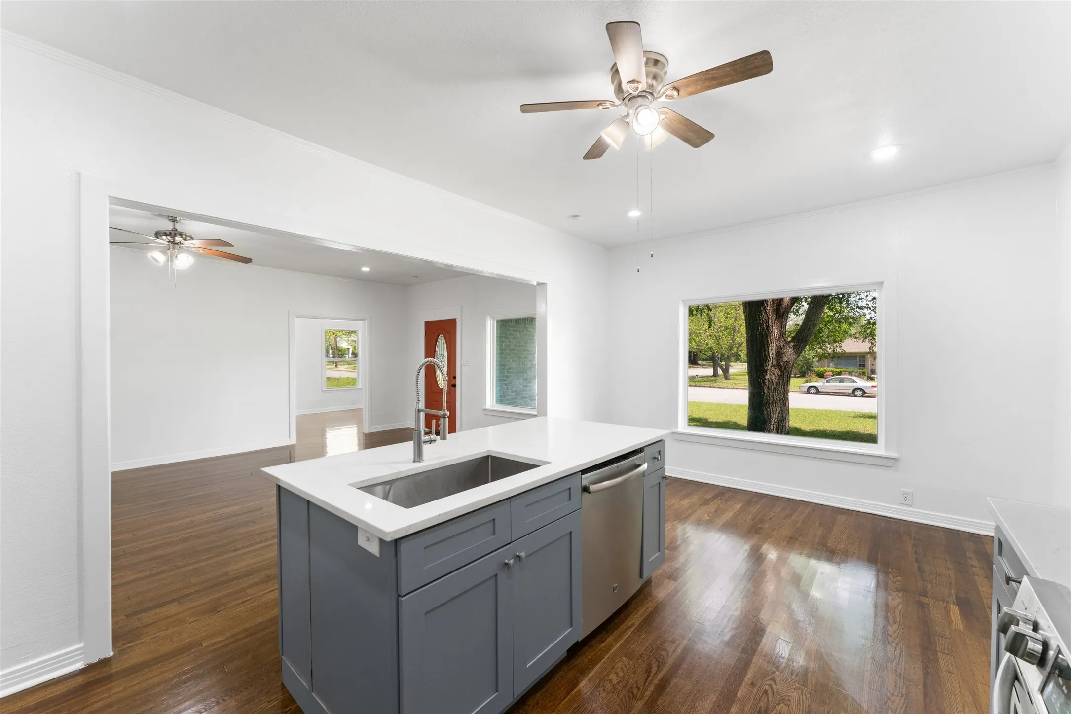 Central kitchen island with gray cabinetry, integrated sink with gooseneck faucet, and stainless steel dishwasher