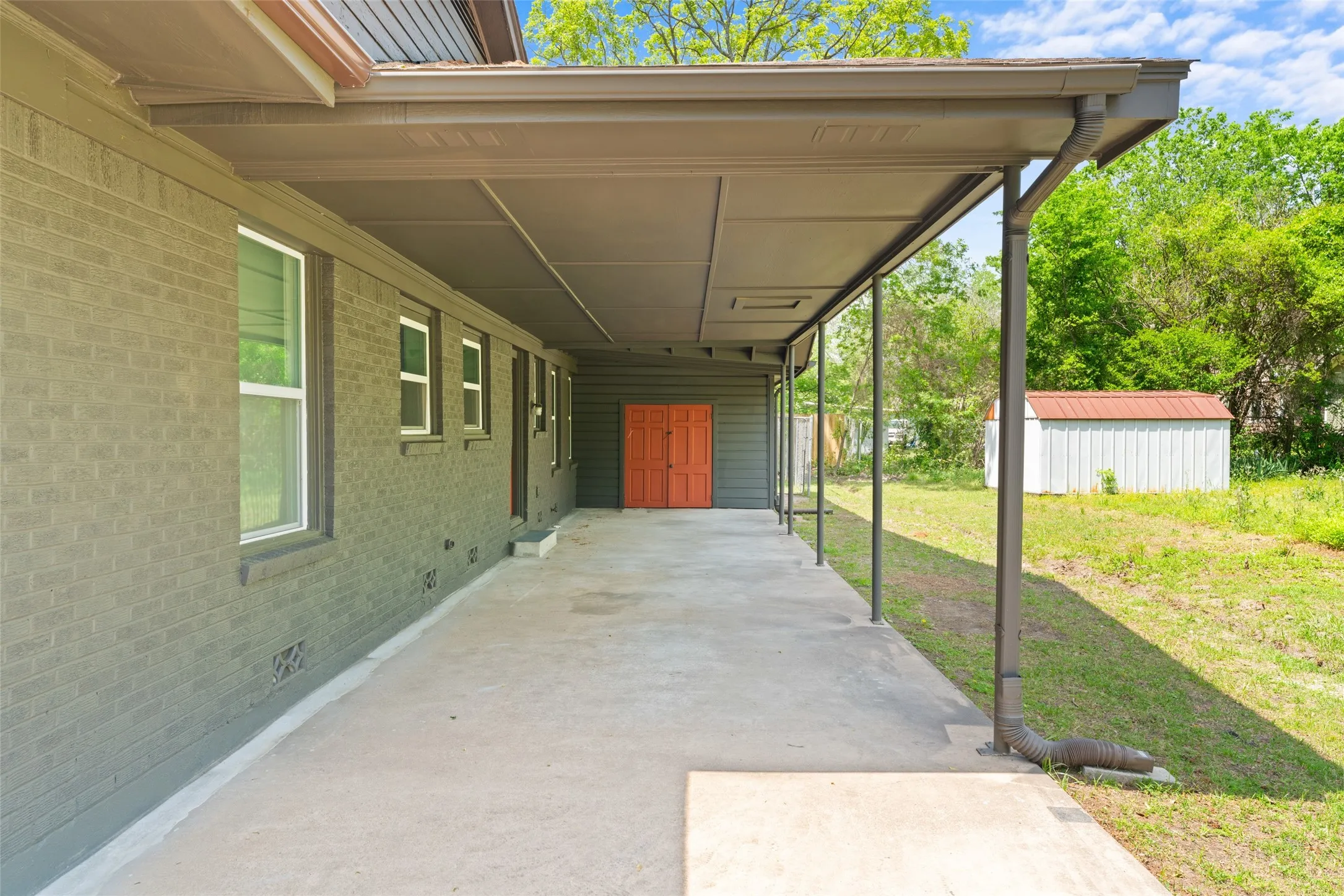 Covered concrete patio with a painted brick exterior and multiple windows