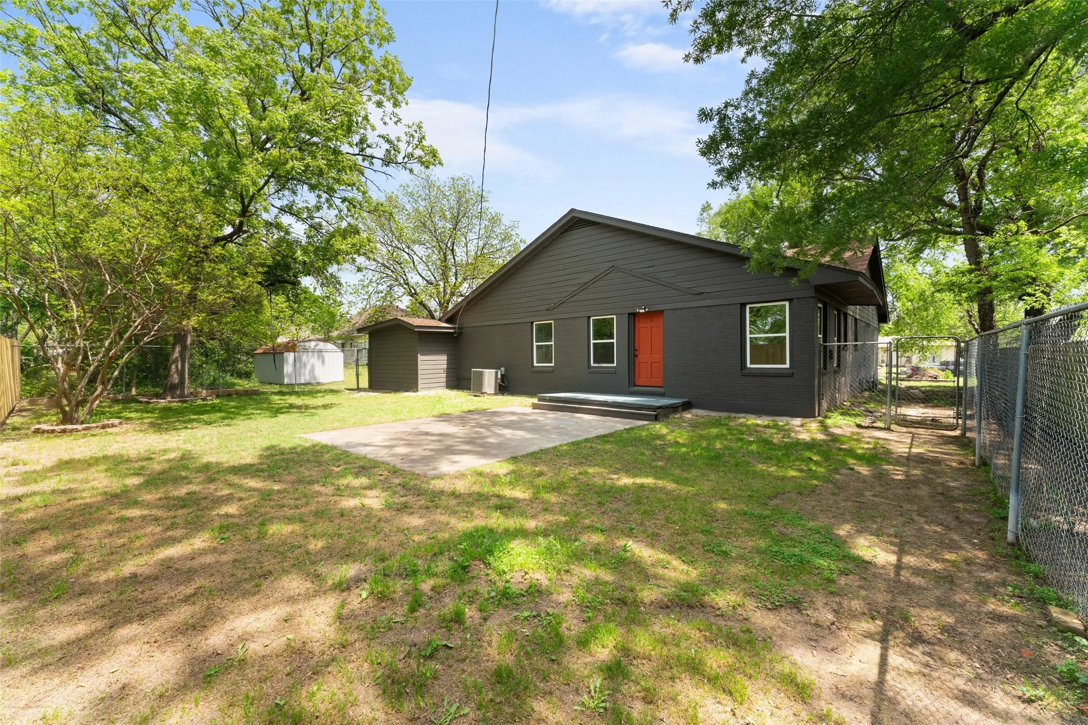 Expansive backyard featuring a concrete patio, mature trees, and a chain-link fence