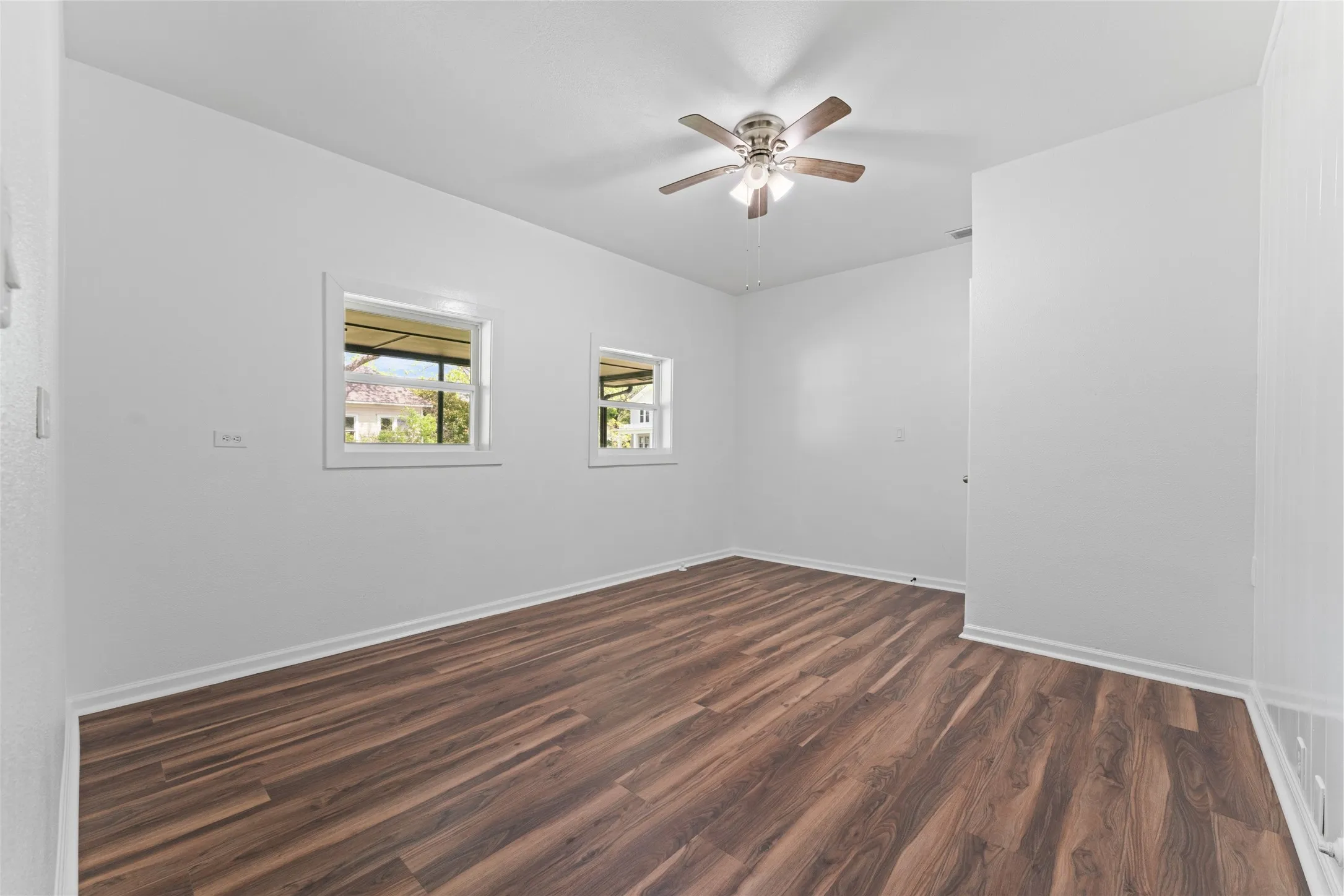 Wood-finish flooring, white walls, two windows, and a ceiling fan with integrated lighting