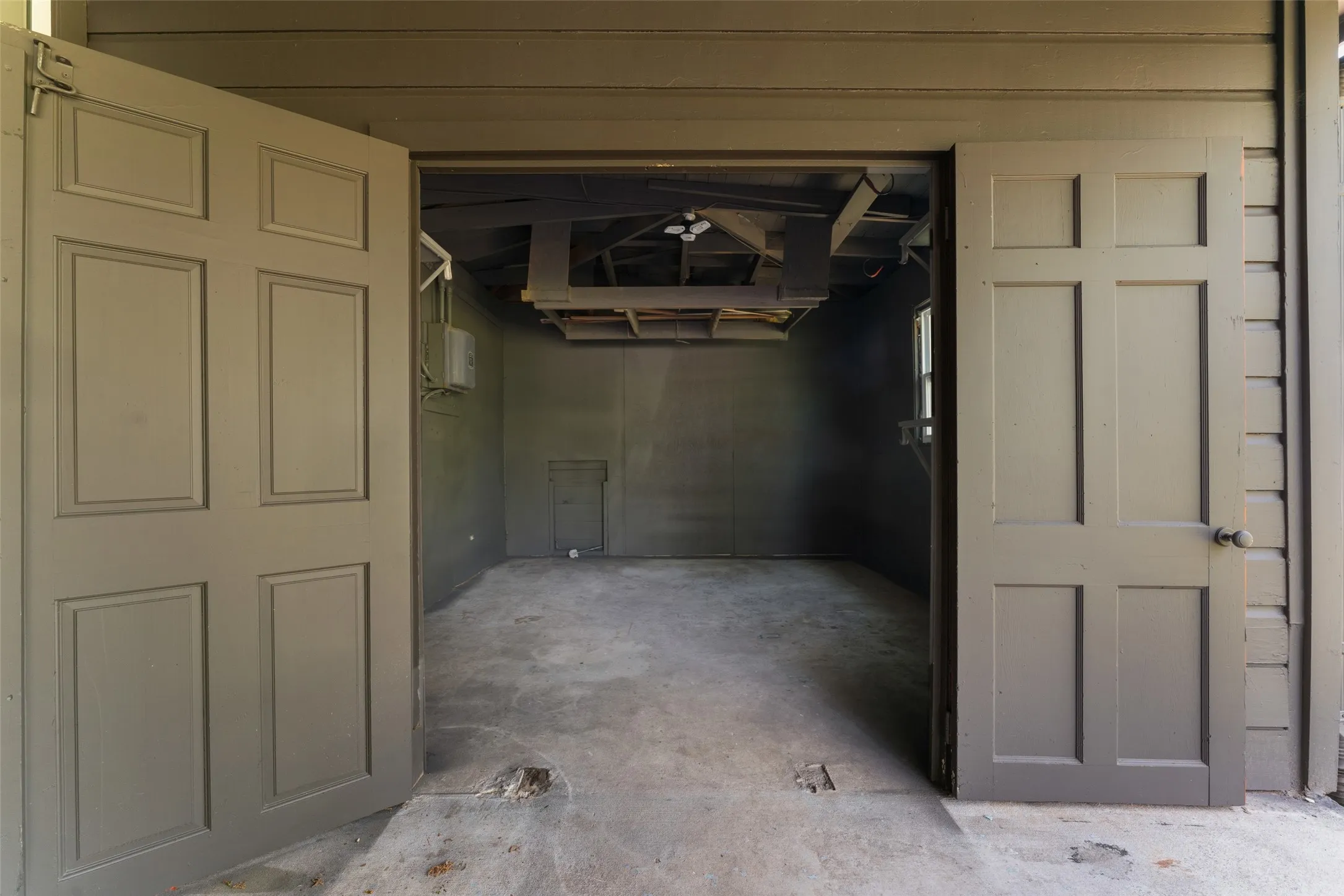 Oversized garage doors with panel detailing, concrete flooring, and exposed ceiling joists