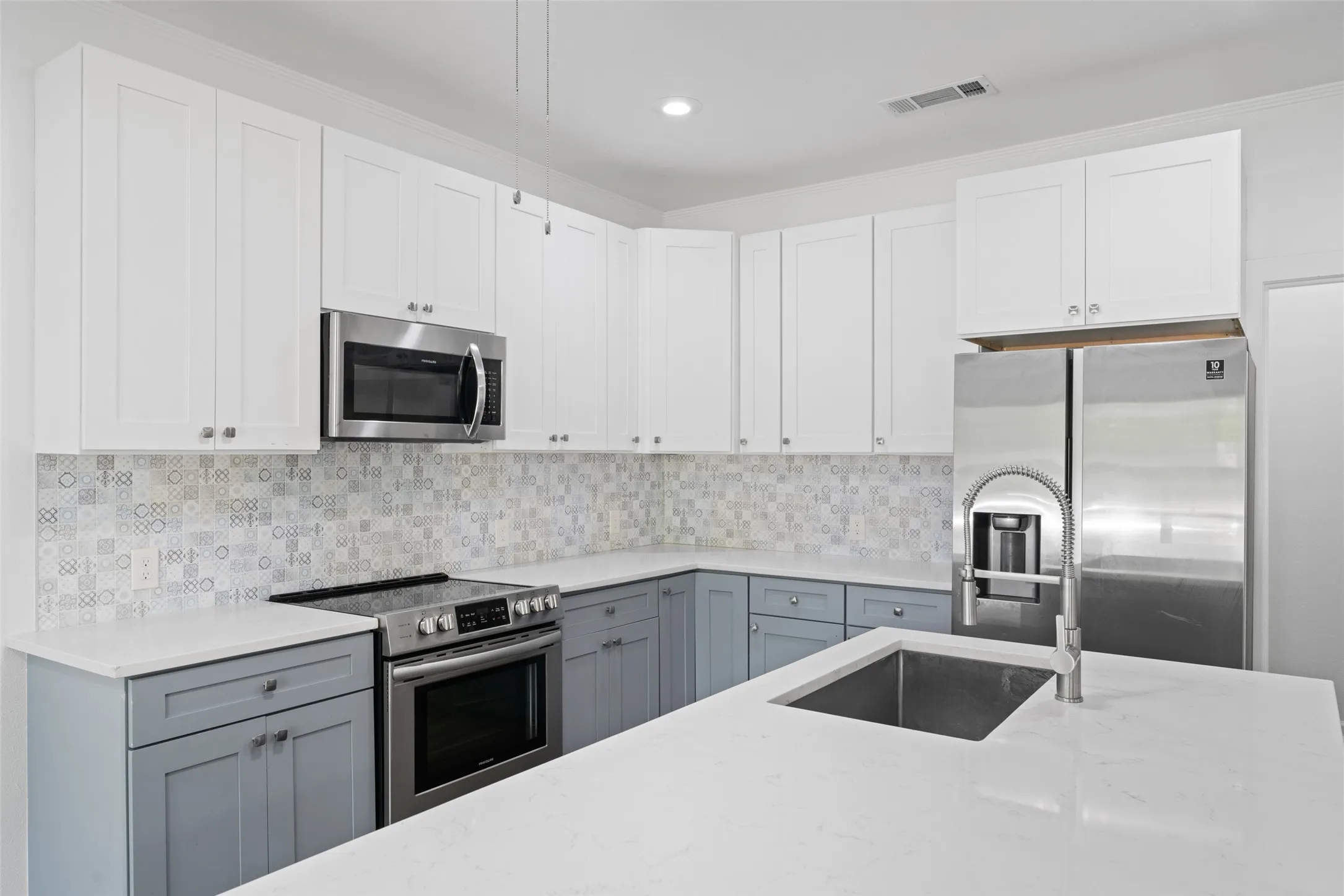 White shaker-style upper cabinetry, stainless steel appliances, patterned tile backsplash, white countertops, and a kitchen island with an undermount sink