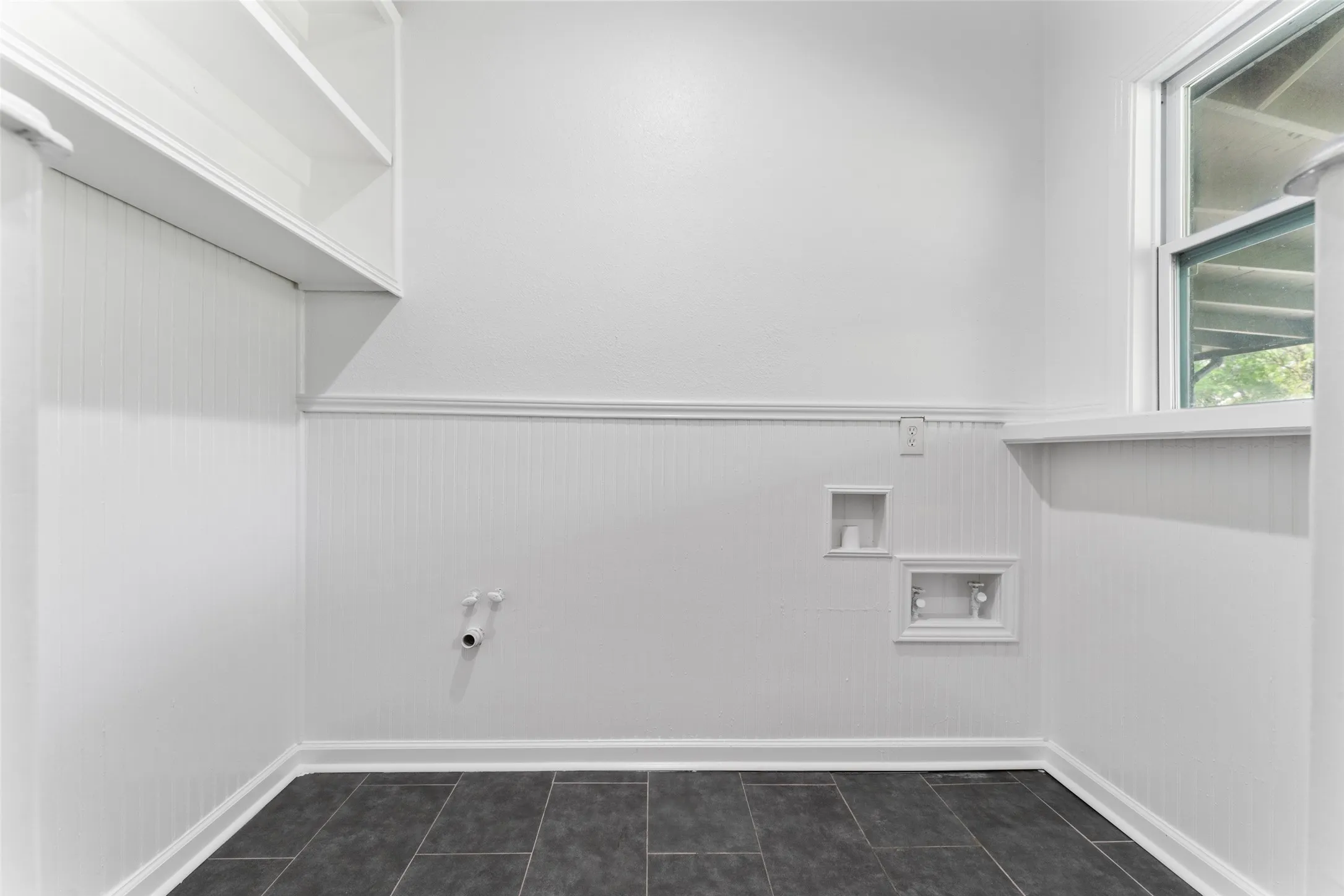 White beadboard paneling, built-in shelving, dark-toned flooring, and a large window