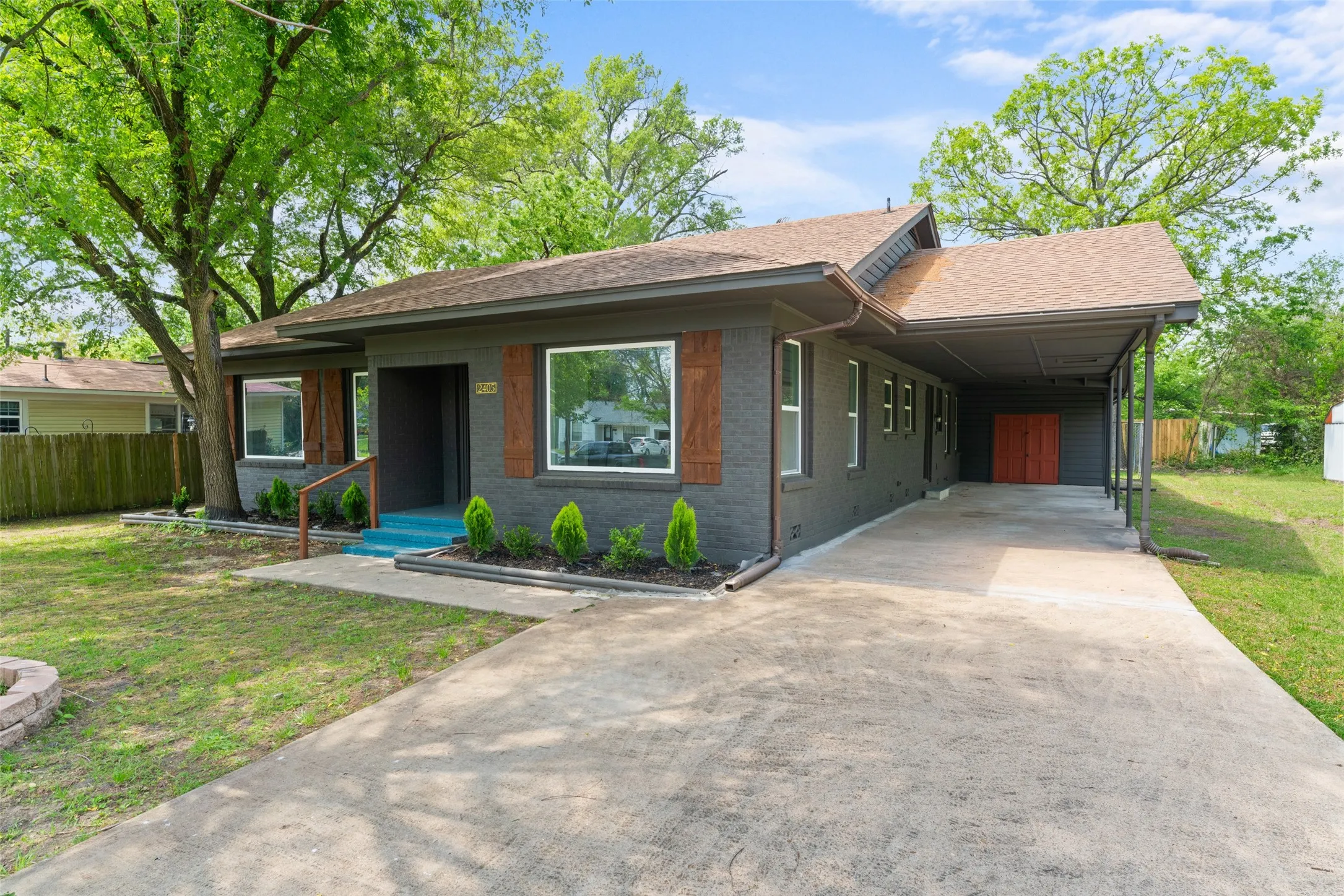 Charcoal exterior with contrasting wood-finish shutters, covered carport, concrete driveway, and established front yard landscaping