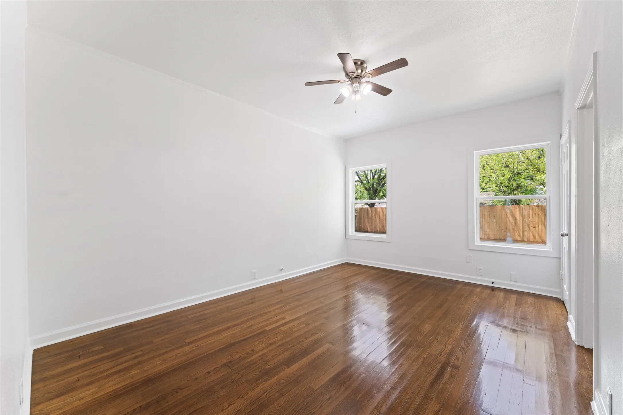 Hardwood flooring, two windows, ceiling fan with integrated lighting, white walls, and white trim
