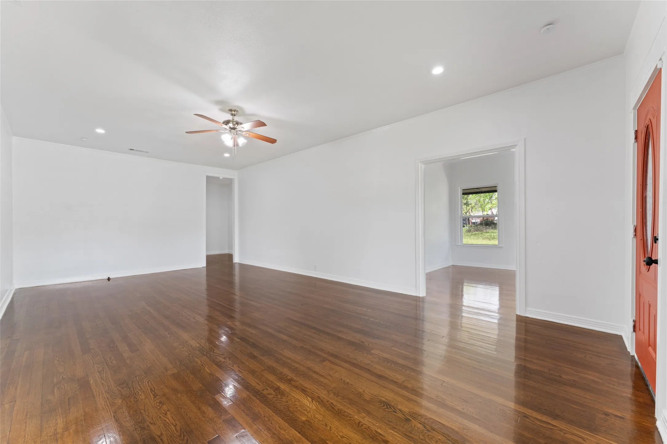 Wood-finish flooring throughout, recessed ceiling lighting, ceiling fan with light fixture, white interior walls, and an orange front entry door