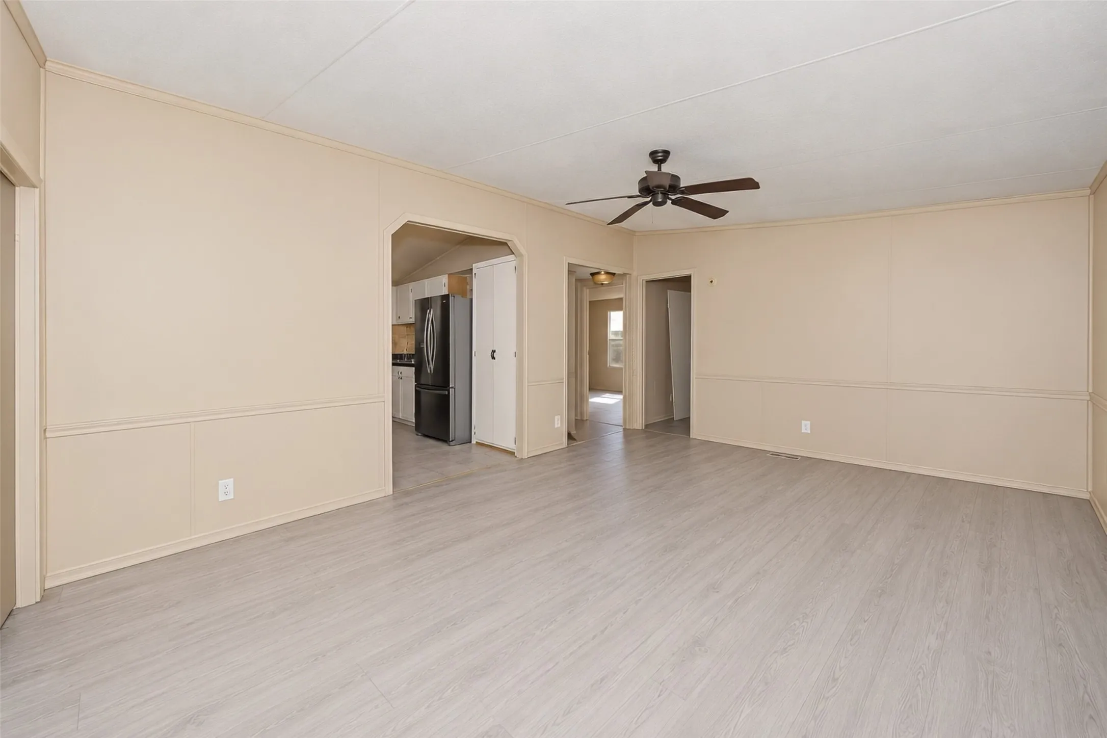 Spacious living area featuring wood-finish flooring, neutral wall tones, wainscoting, and a ceiling fan
