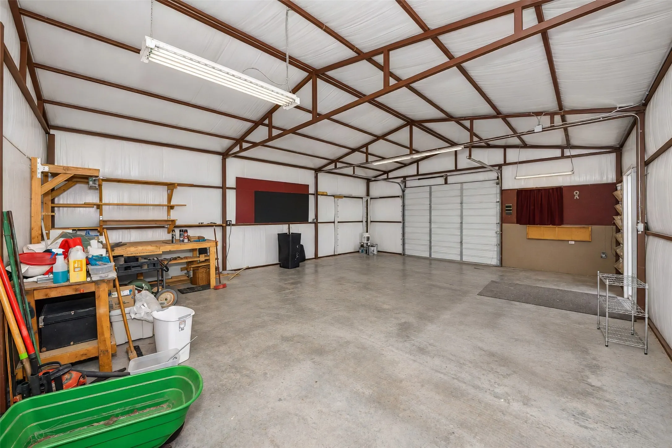 Spacious metal-frame building featuring a concrete floor, built-in shelving, and a large roll-up door
