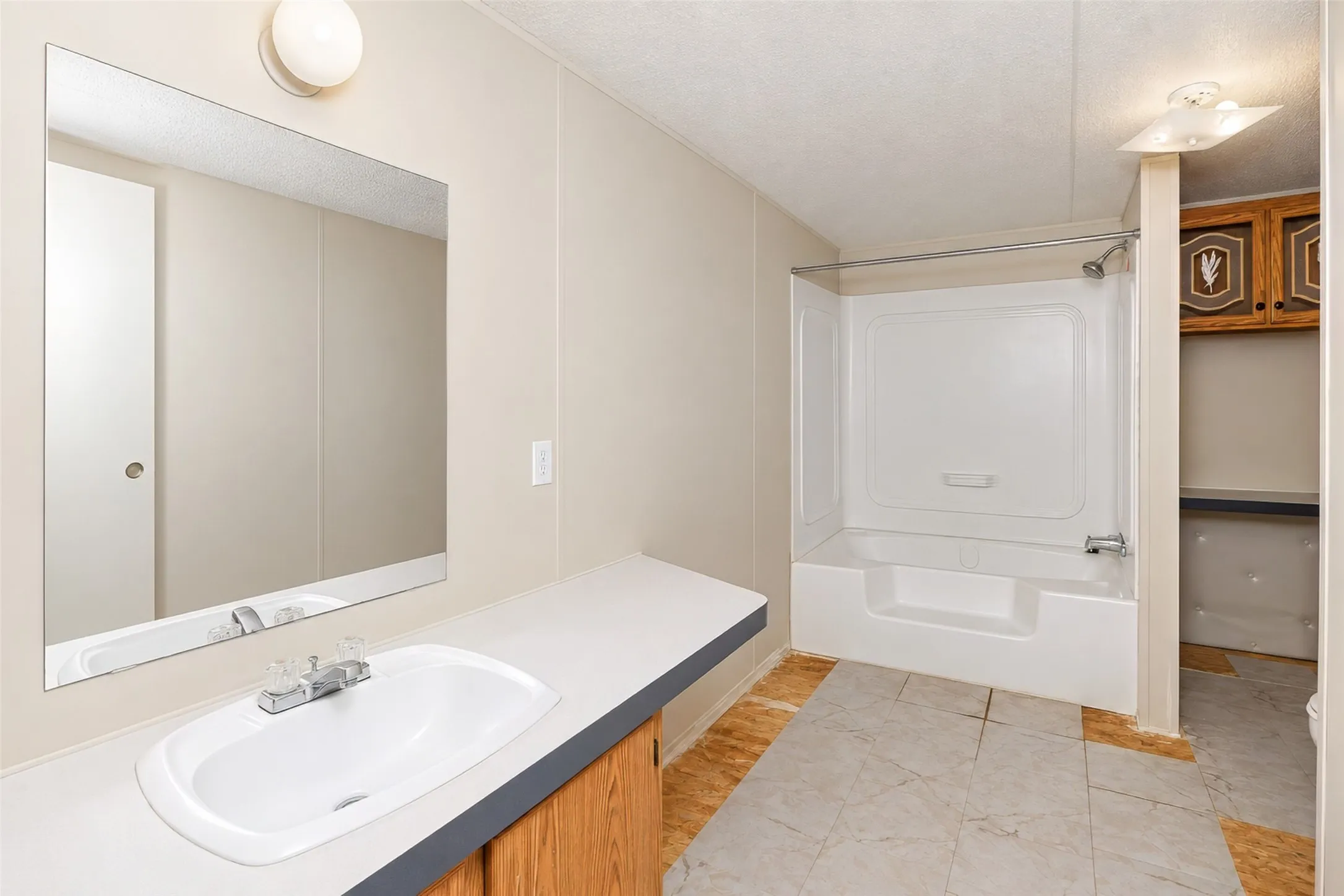 White drop-in sink with a laminate countertop, mirrored wall feature, and a white tub/shower combination with a chrome showerhead
