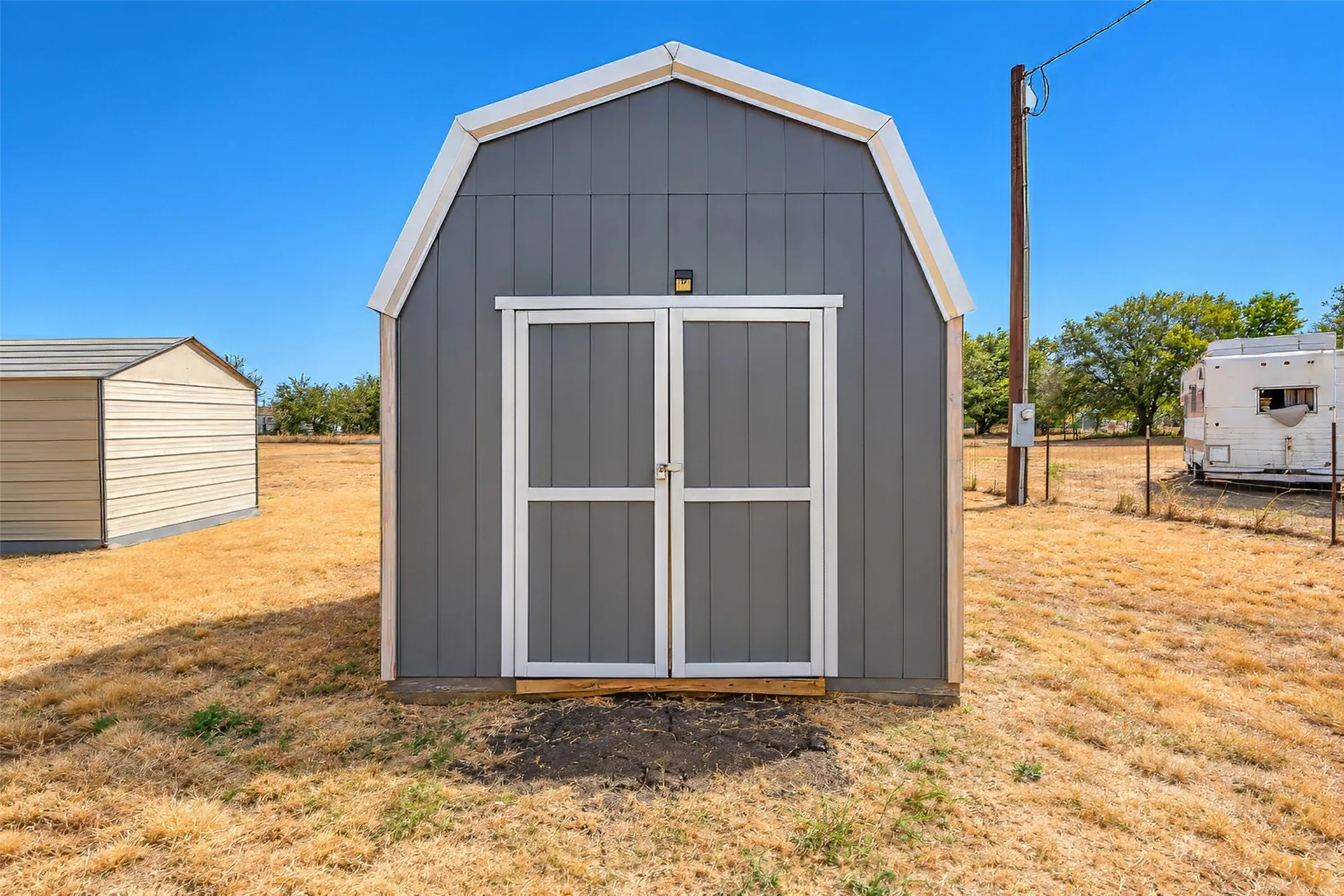 Gray gambrel-style shed with white trim and double doors