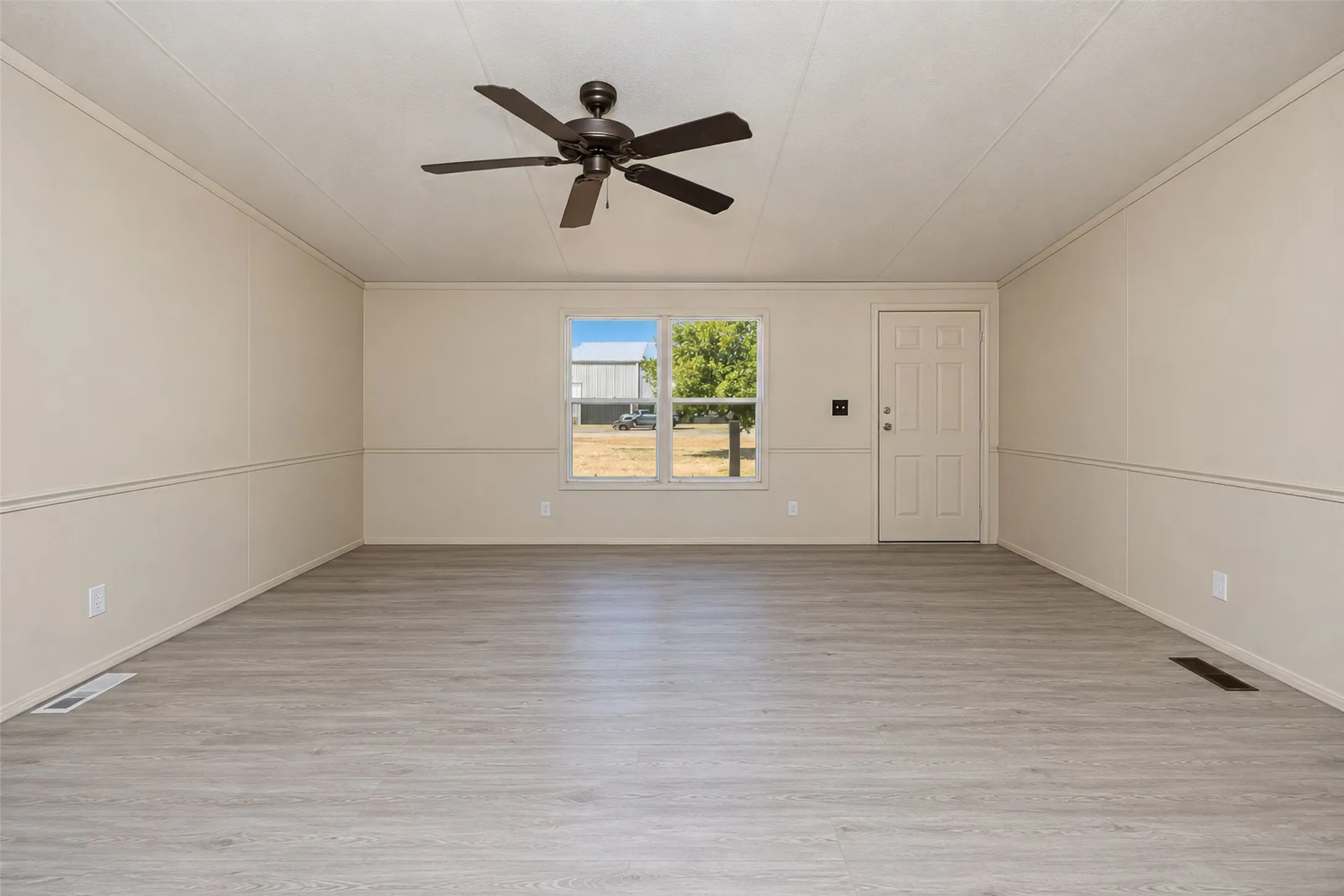 Spacious interior featuring wood-finish flooring, a ceiling fan, and paneled walls with chair rail detailing