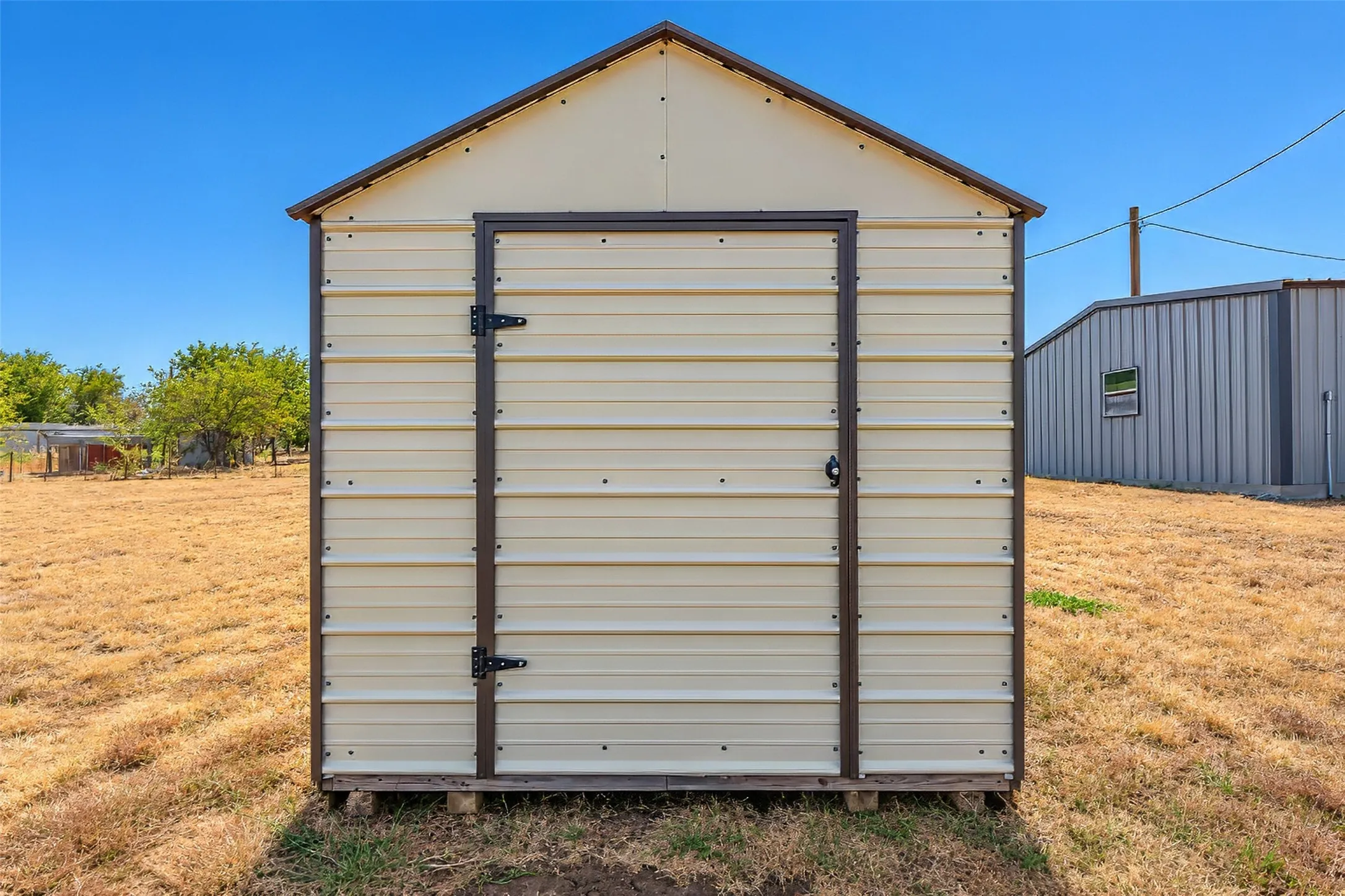 Metal shed featuring a peaked roof, double doors, and a neutral color palette