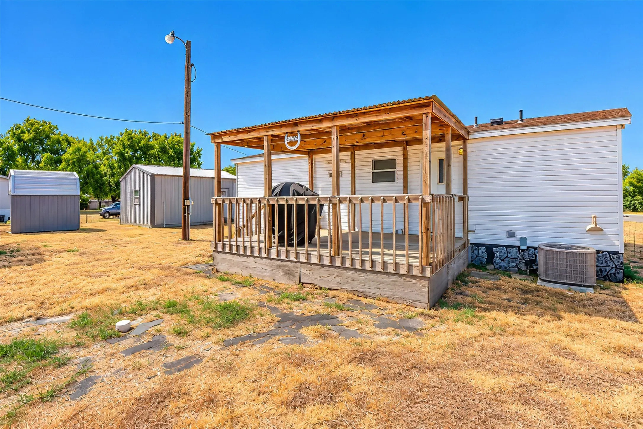 Covered wooden deck with railing, white siding exterior, and adjacent metal outbuilding