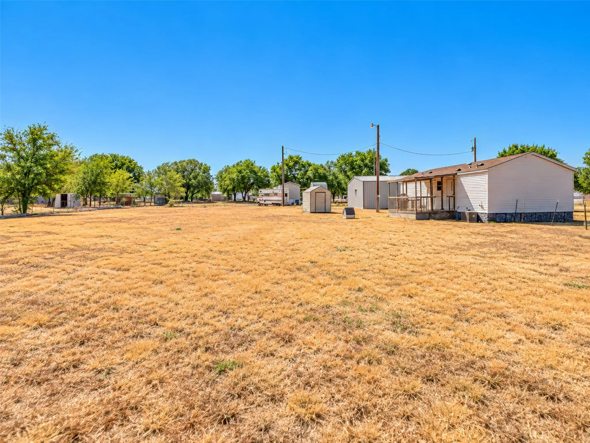 Expansive yard area with established trees, a white-sided residence, covered porch, and two detached storage structures