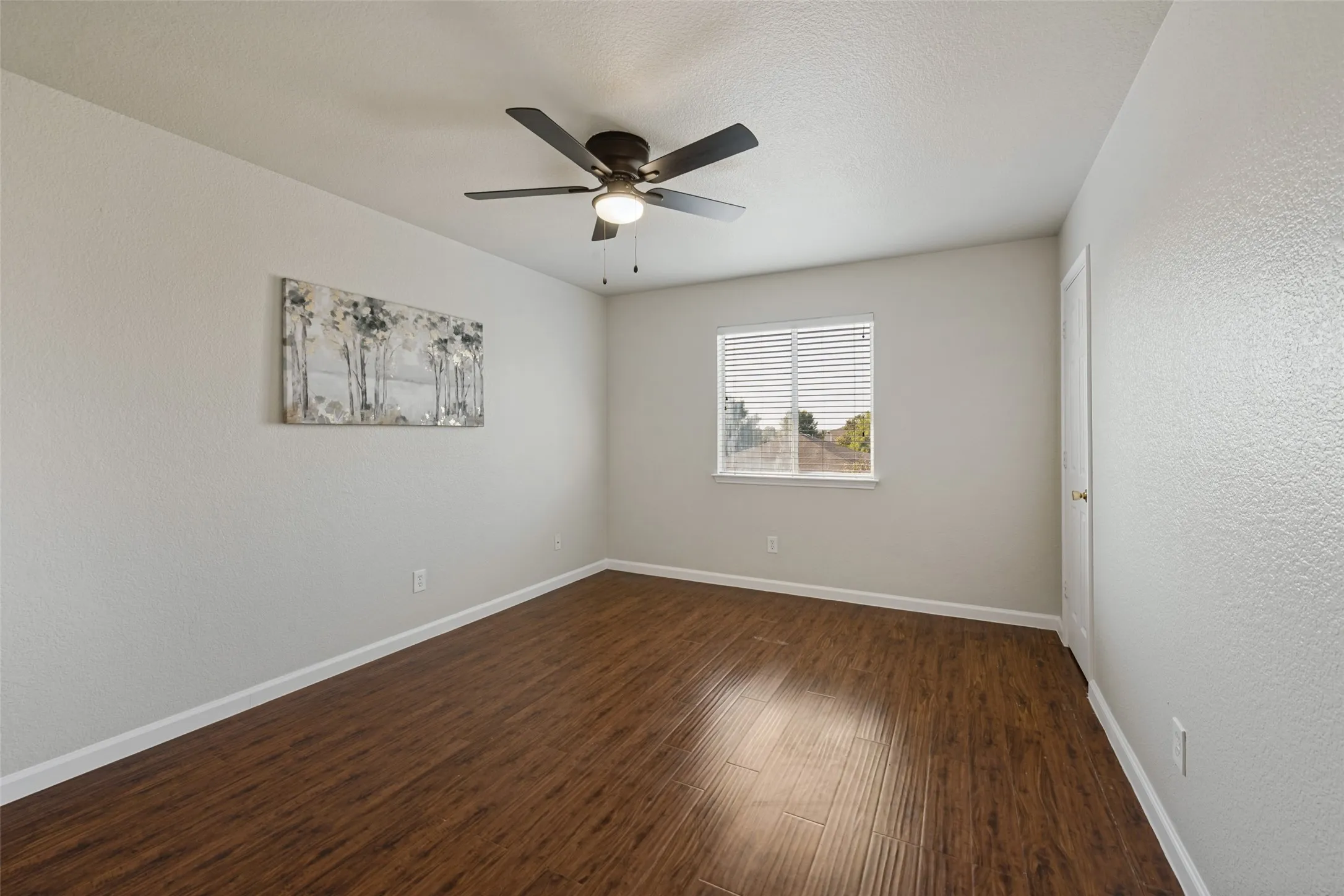 Wood-finish flooring, light neutral-toned walls, and a ceiling fan with integrated lighting