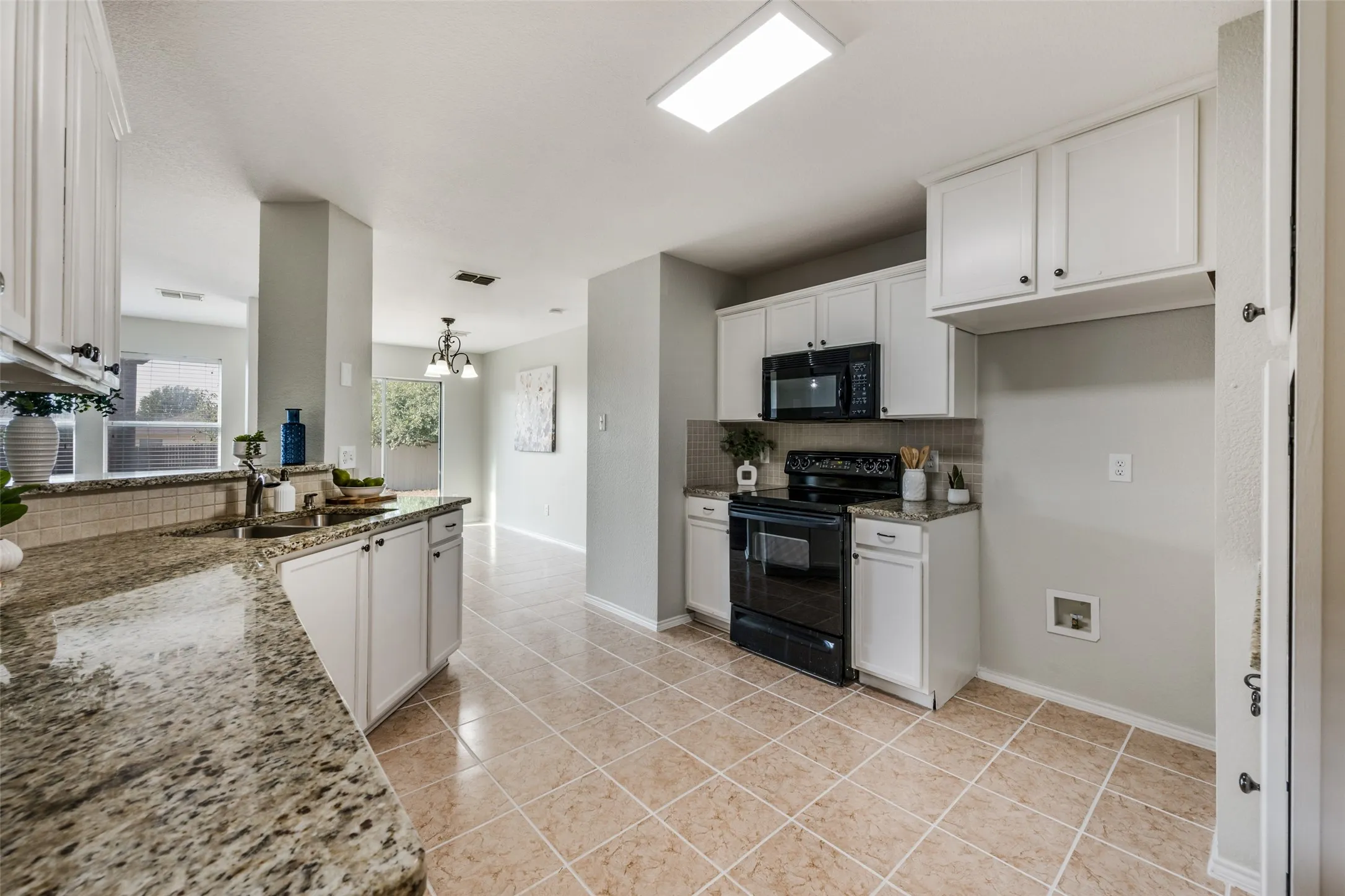 Kitchen featuring a black electric range, black built-in microwave, white cabinetry with dark hardware, a double basin sink, and tile flooring