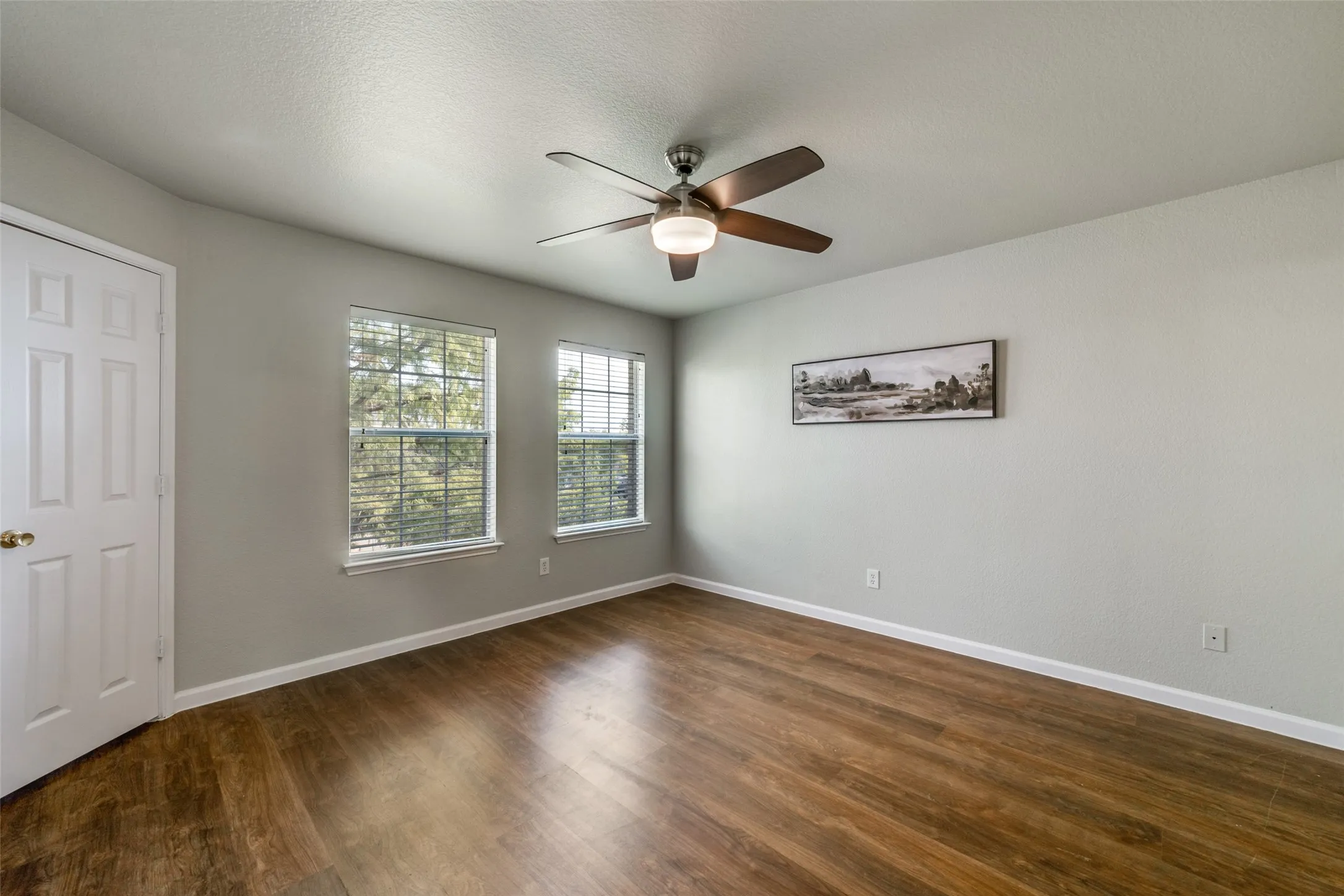 Wood-finish flooring, dual windows with blinds, ceiling fan with integrated lighting, and a paneled door