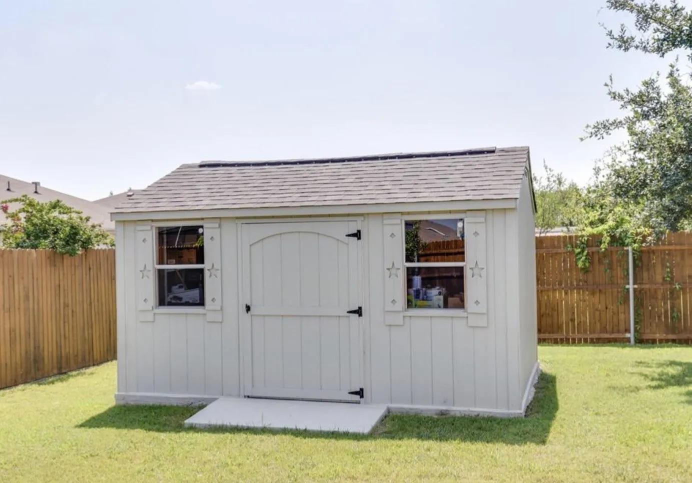 Wood-paneled storage shed with a shingle roof, two windows, and a concrete landing