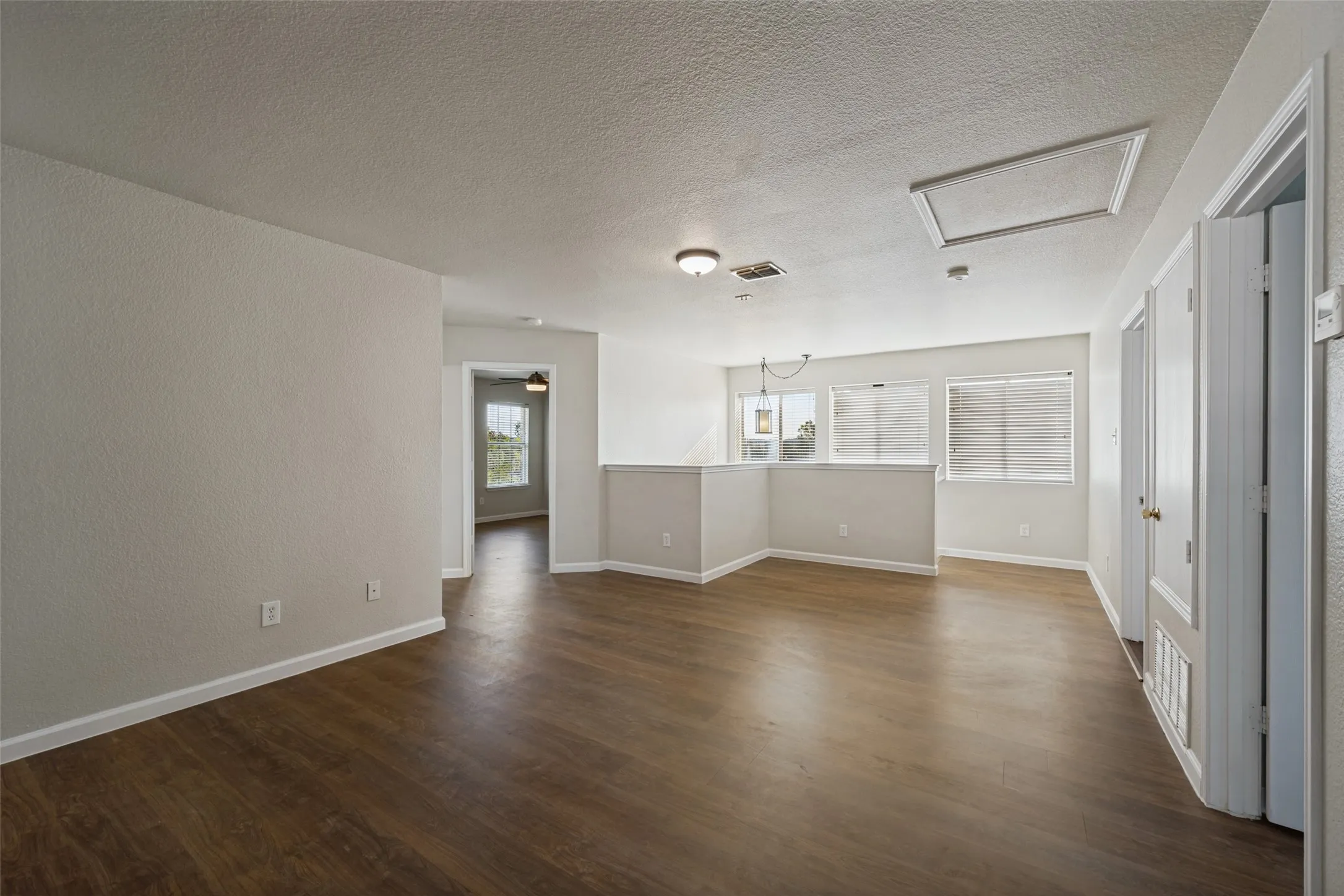 Expansive room featuring wood-finish flooring, white walls, multiple windows with blinds, and flush-mount lighting