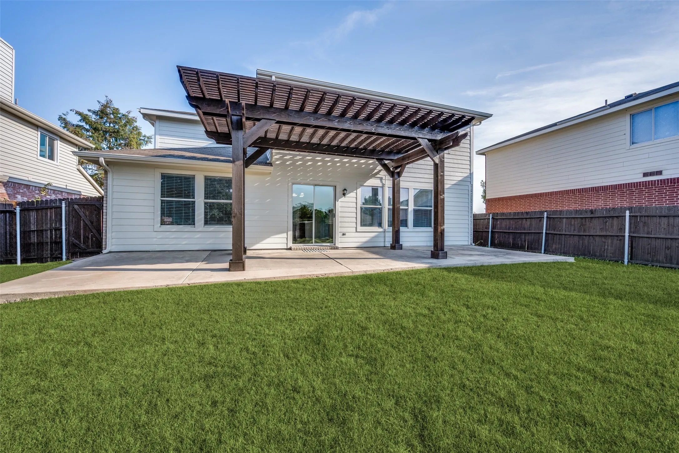 Expansive backyard featuring a pergola-covered patio, sliding glass door, and a privacy fence
