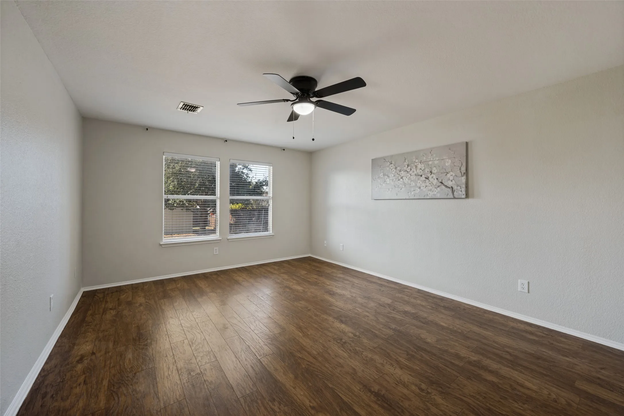 Wood-finish flooring, two windows with blinds, and a ceiling fan with integrated lighting