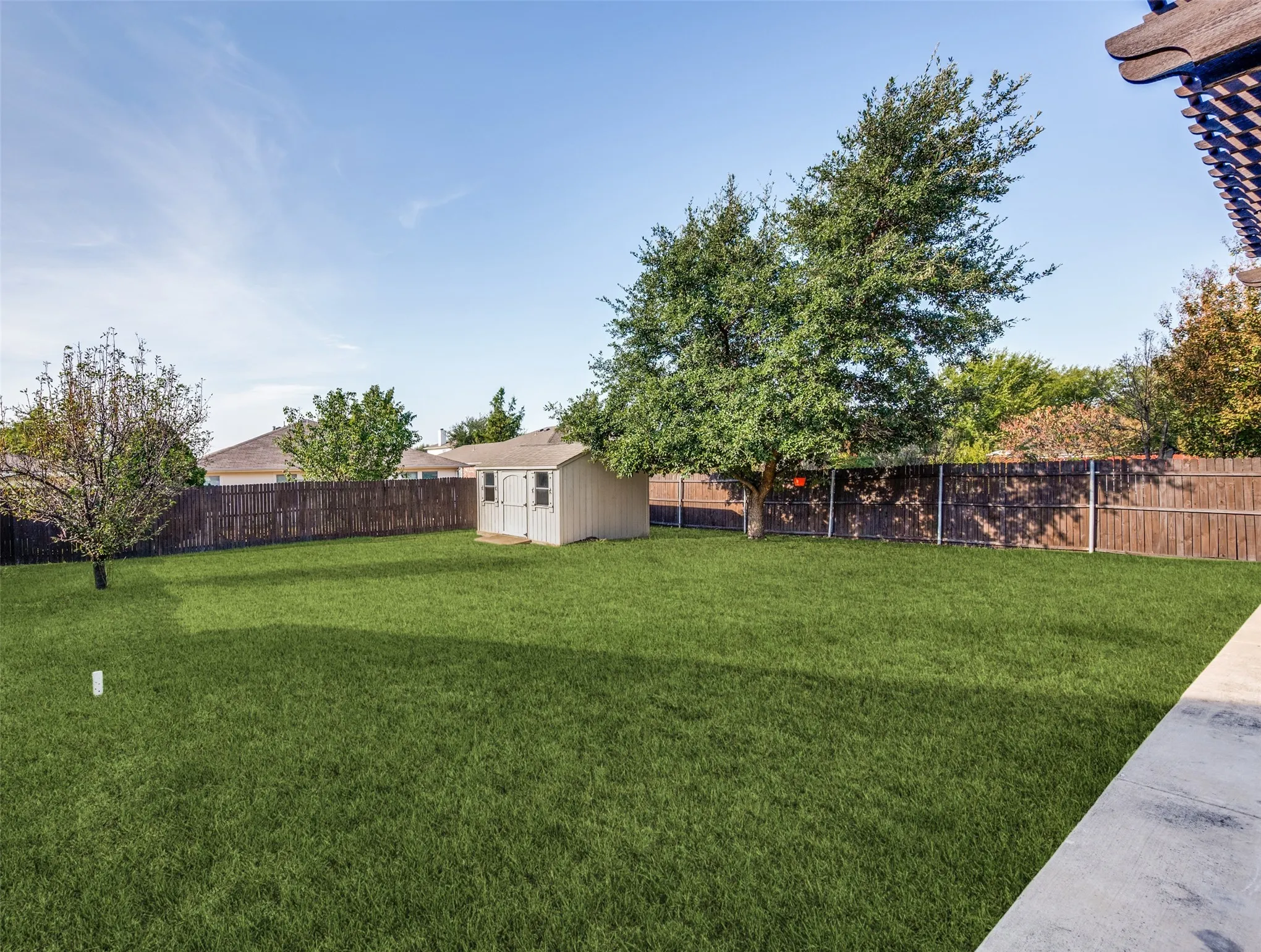 Expansive backyard featuring a manicured lawn, a detached storage shed, mature trees, and a wood privacy fence