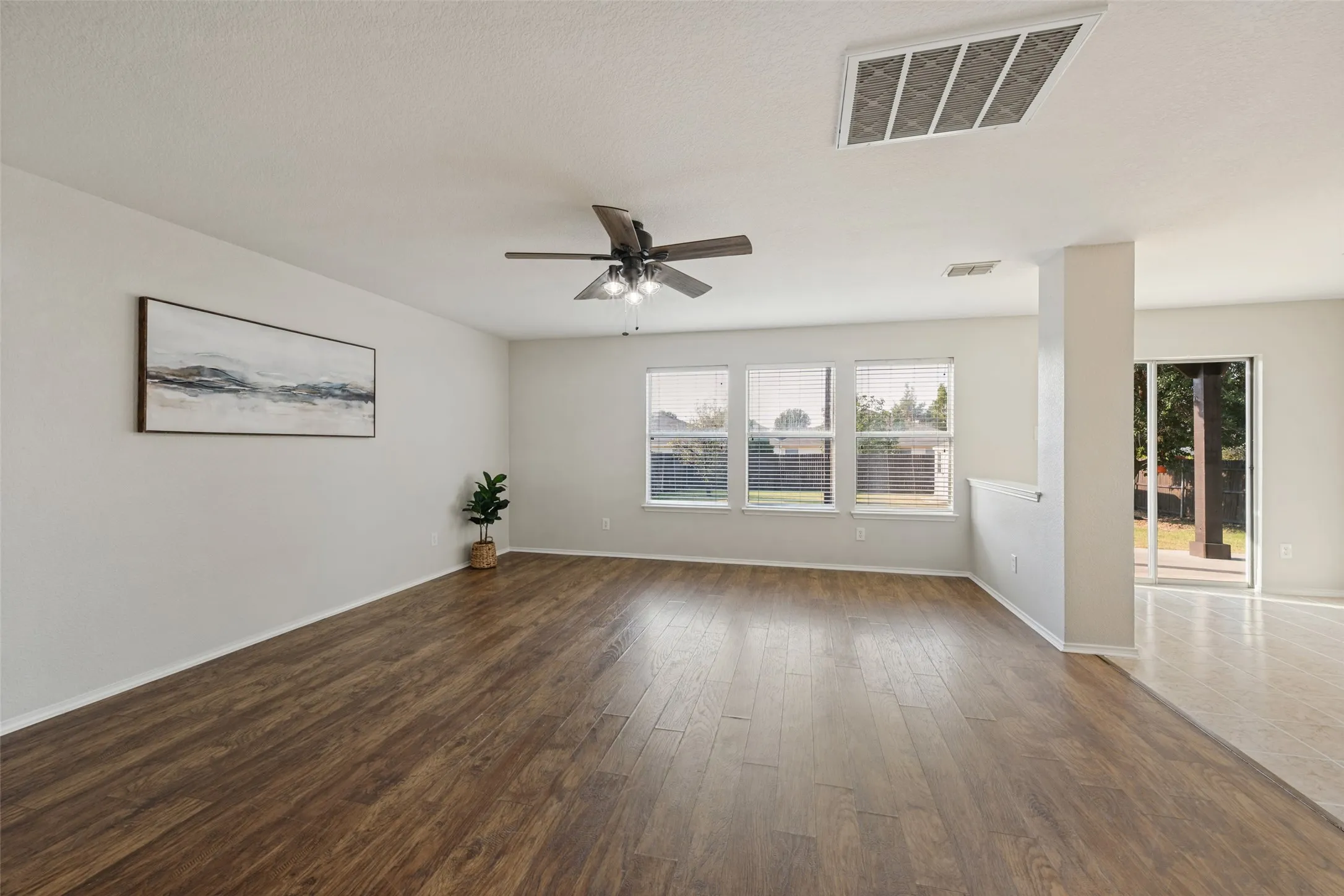 Spacious living area featuring wood-finish flooring, multiple windows, a ceiling fan, and a sliding glass door