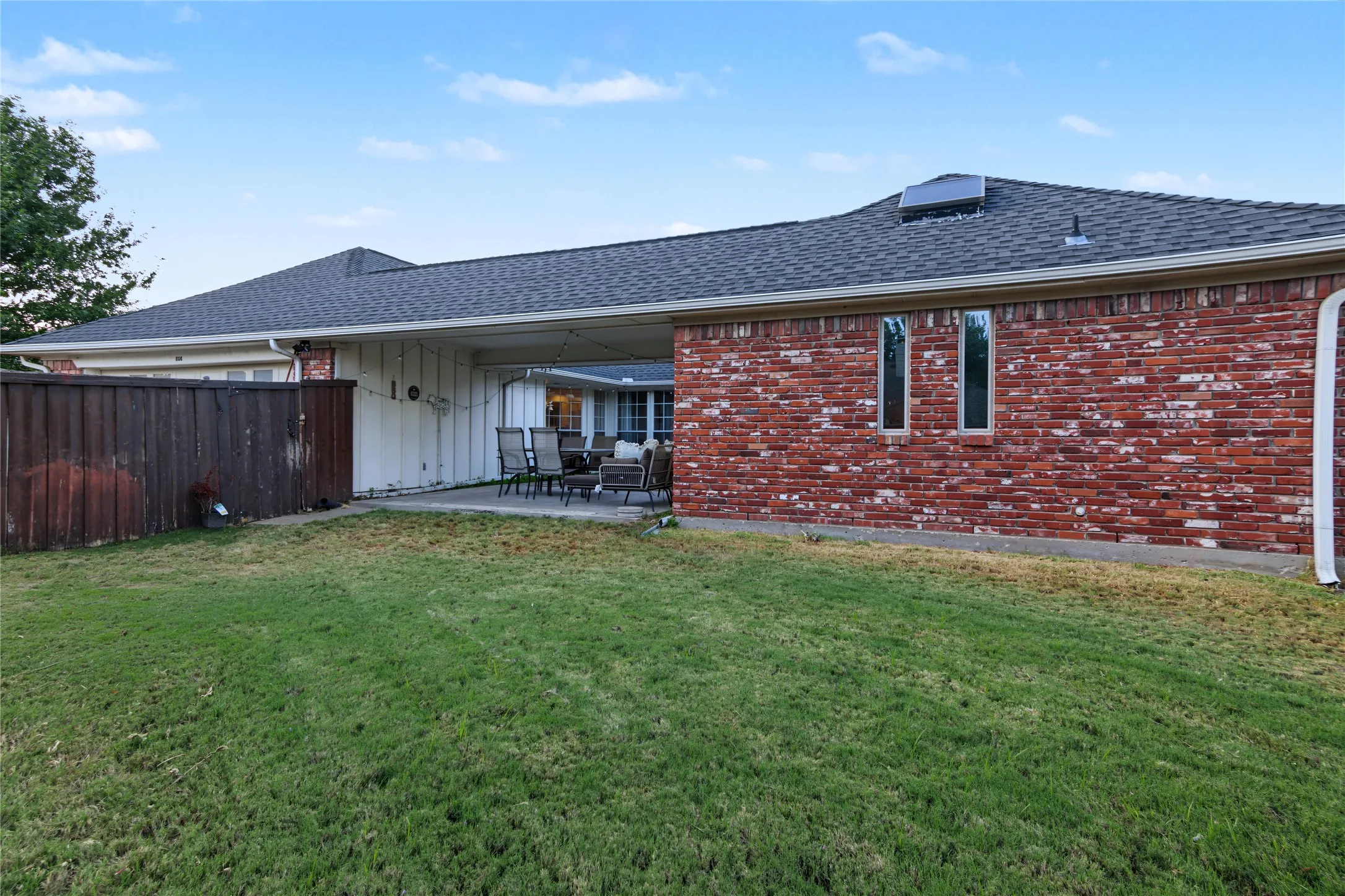 Manicured lawn with a privacy fence, brick exterior, and covered patio