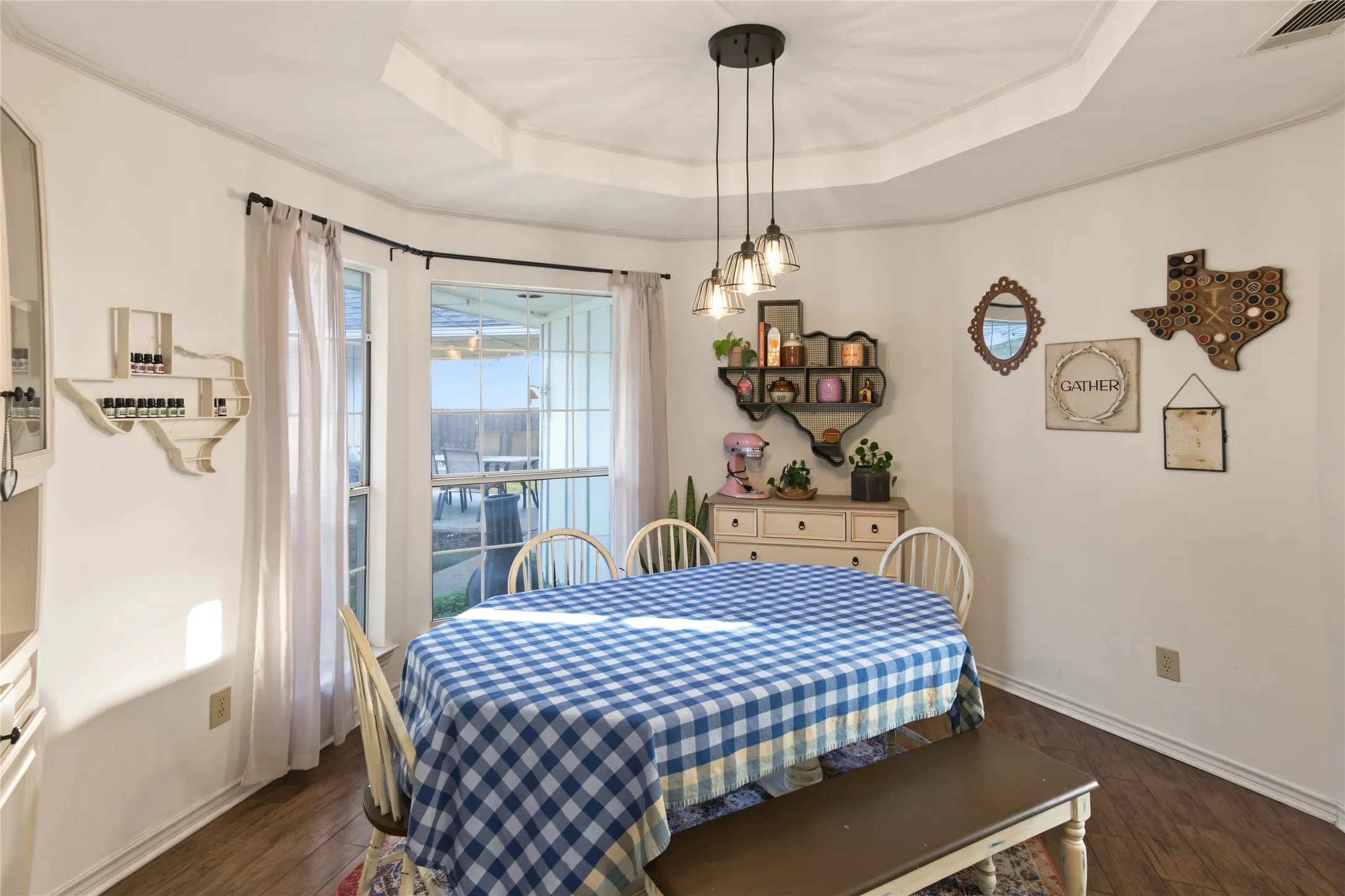 Bay window with outdoor visibility, tray ceiling, wood-finish flooring, and a multi-light pendant fixture