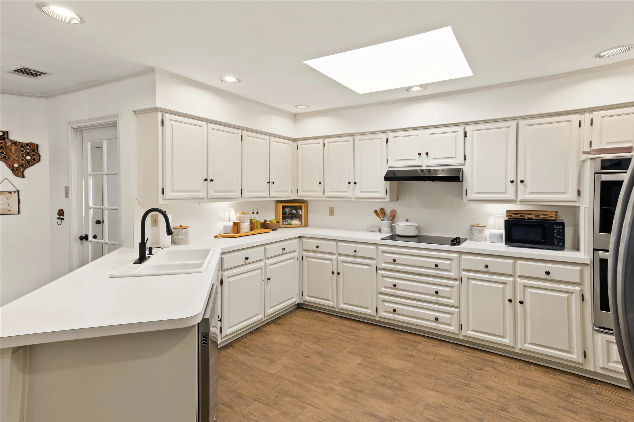Spacious kitchen featuring extensive white cabinetry, light-toned countertops, wood-finish flooring, a contemporary black faucet, and recessed lighting