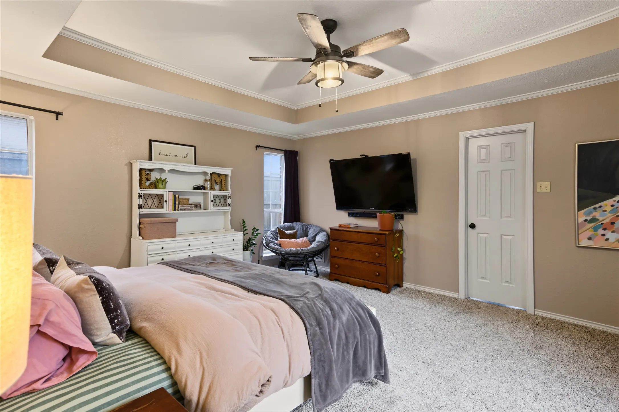 Tray ceiling with crown molding, ceiling fan with light fixture, carpeted flooring, and a white paneled door