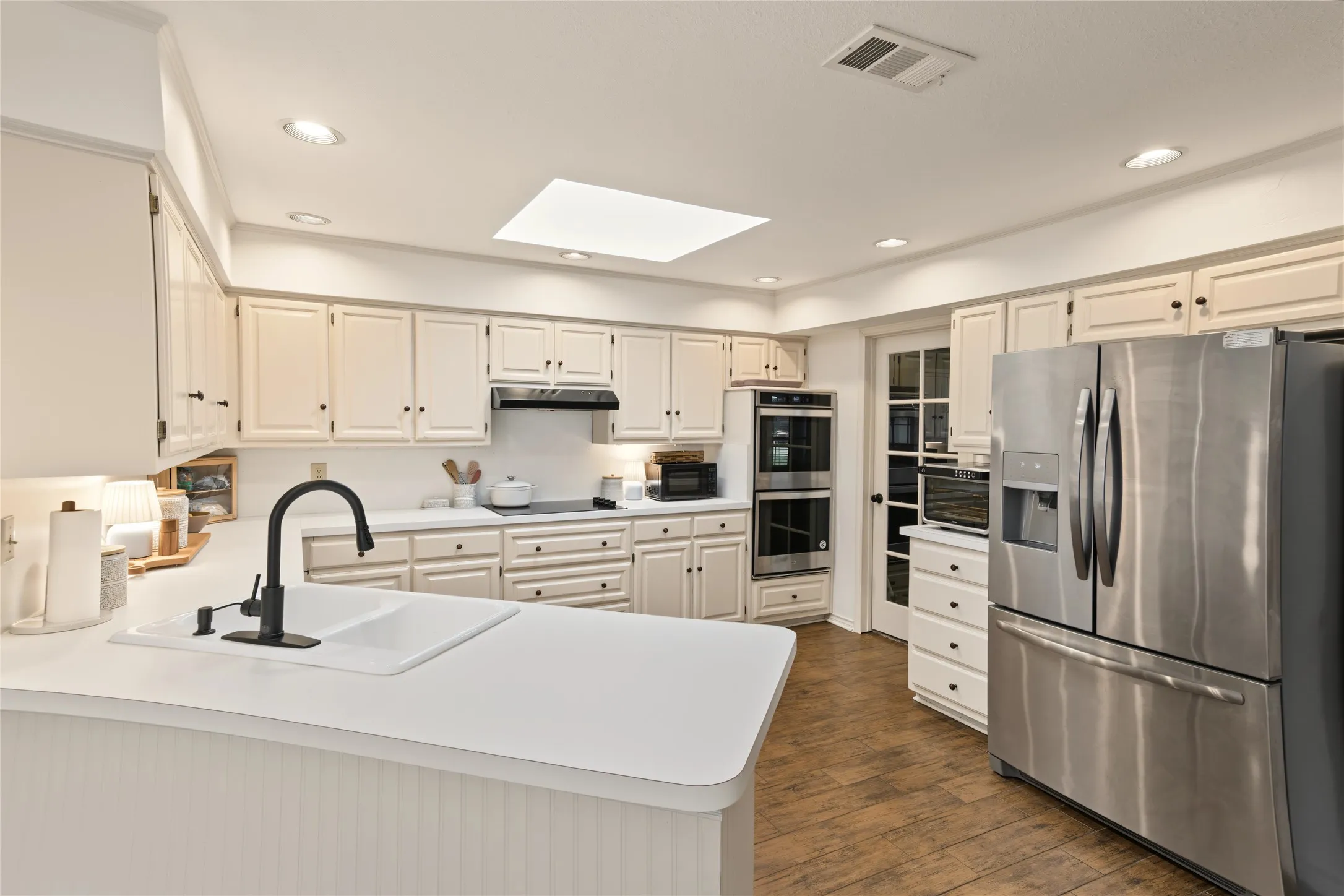 Kitchen featuring wood-finish flooring, white cabinetry, a skylight, and stainless steel double ovens